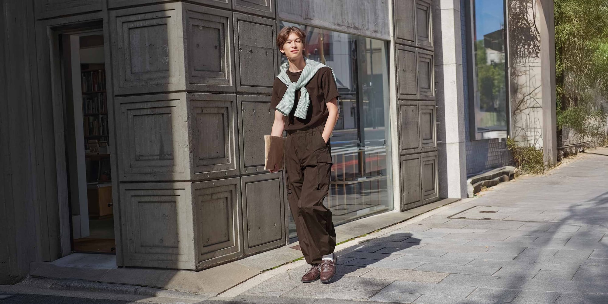 model wearing Wide Cargo Trousers in dark brown with brown T-shirt and shoes and a striped shirt draped over the shoulders
