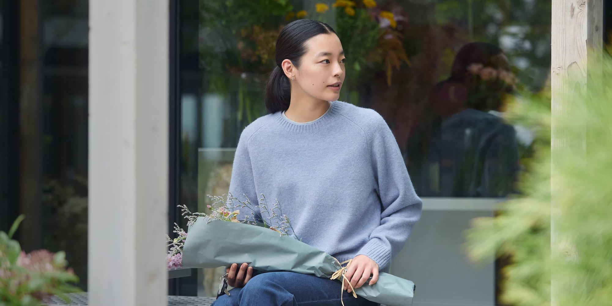 model wearing Soufflé Yarn Crew Neck Jumper in blue with jeans while sat holding a bunch of flowers