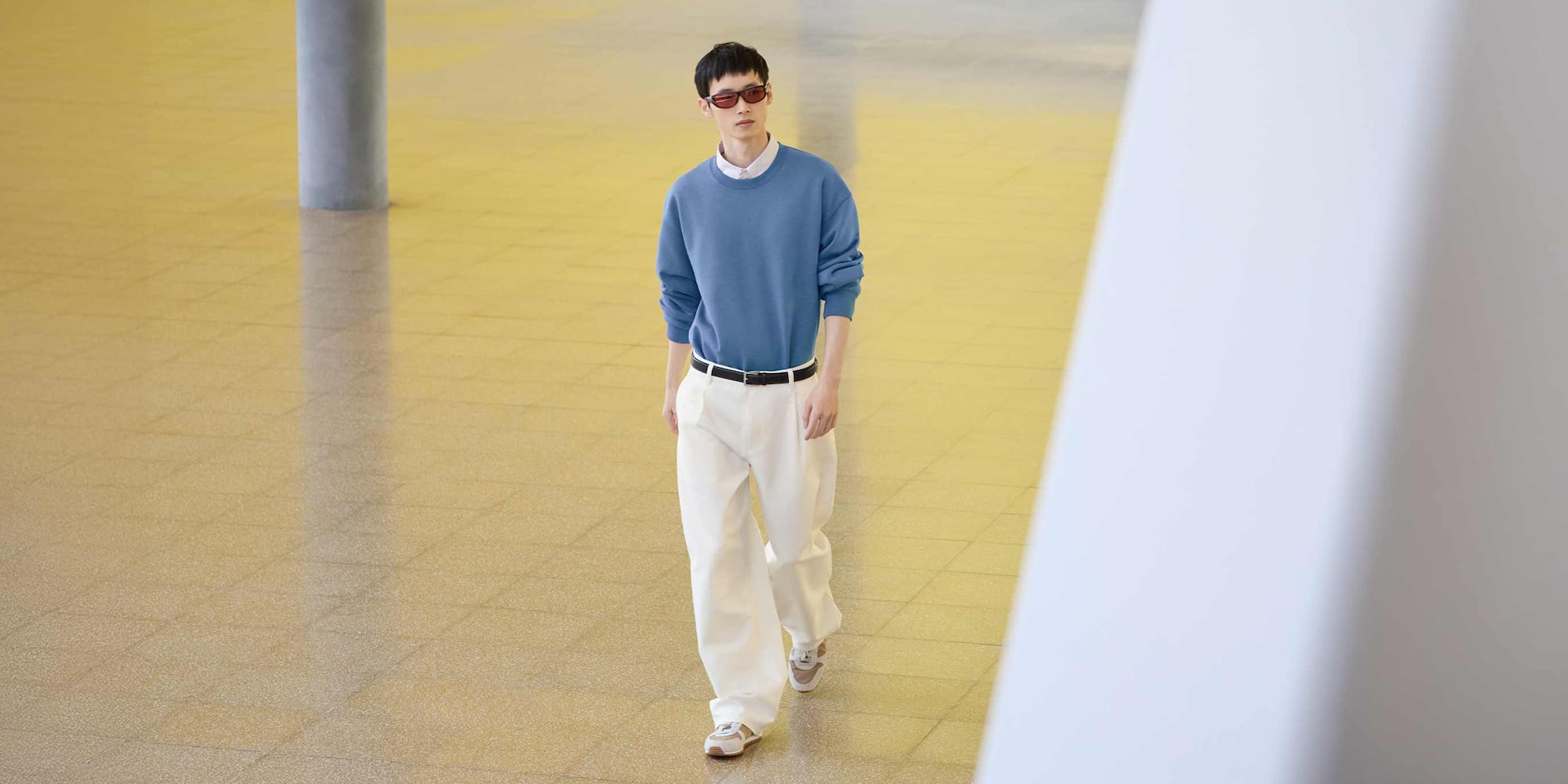 model wearing Barrel Leg Trousers in off white with a blue knit over a white shirt, black belt, brown and white trainers and sunglasses