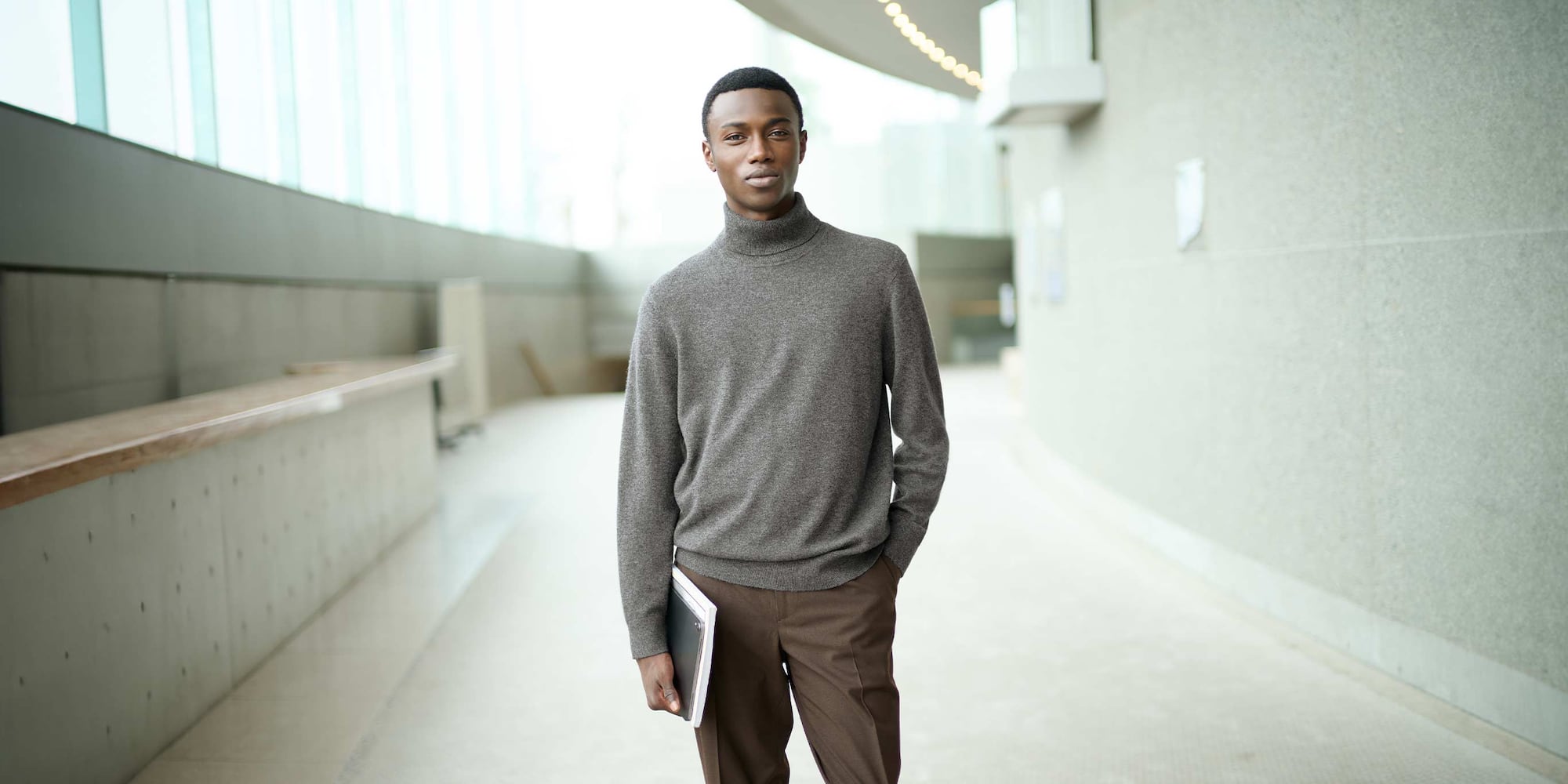 model wearing 100% Cashmere Turtleneck Jumper in grey with brown trousers holding a notebook