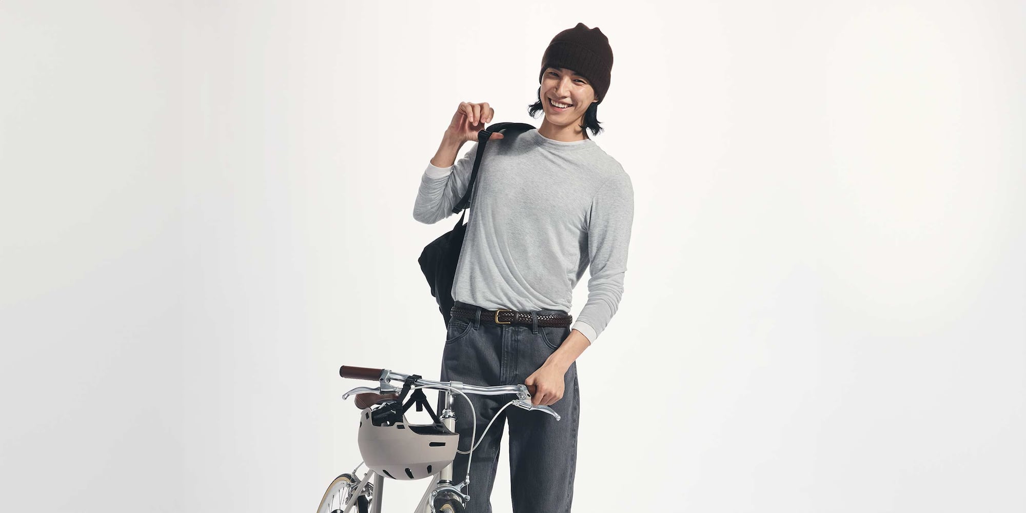 model wearing HEATTECH Extra Warm Cashmere Blend Crew Neck T-Shirt in grey with dark grey jeans and a brown belt while pushing a bike