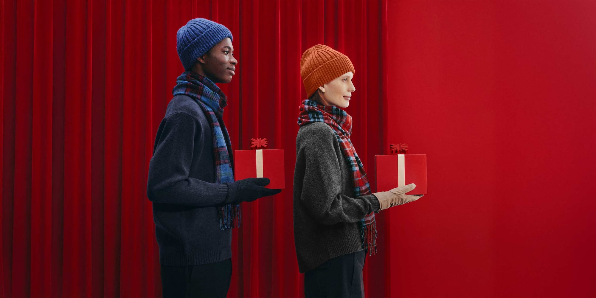 two models wearing UNIQLO hats, scarves and gloves and holding wrapped gifts
