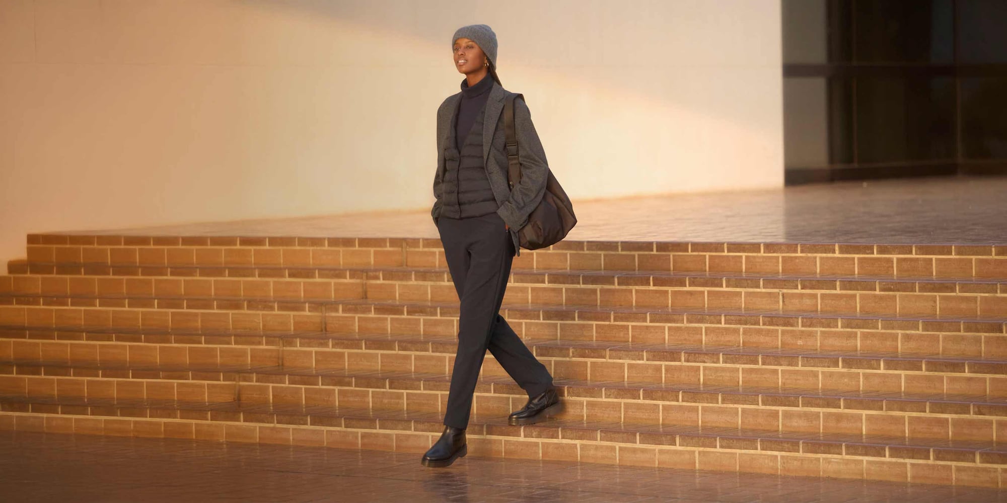 model wearing Warm Stretch Trousers in dark grey with a dark grey turtleneck and dark grey quilted jacket