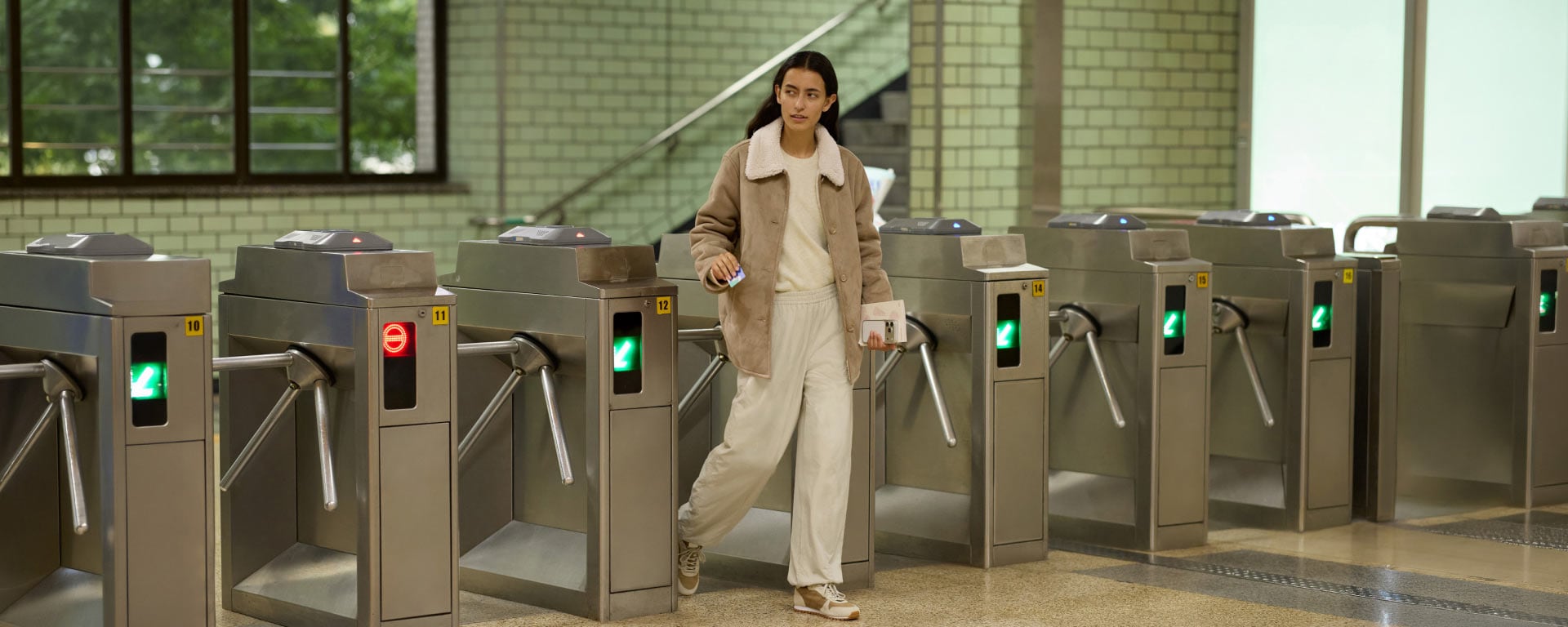 model wearing Fleece Lined Short Coat in beige over an off white top and joggers while walking through a metro turnstile