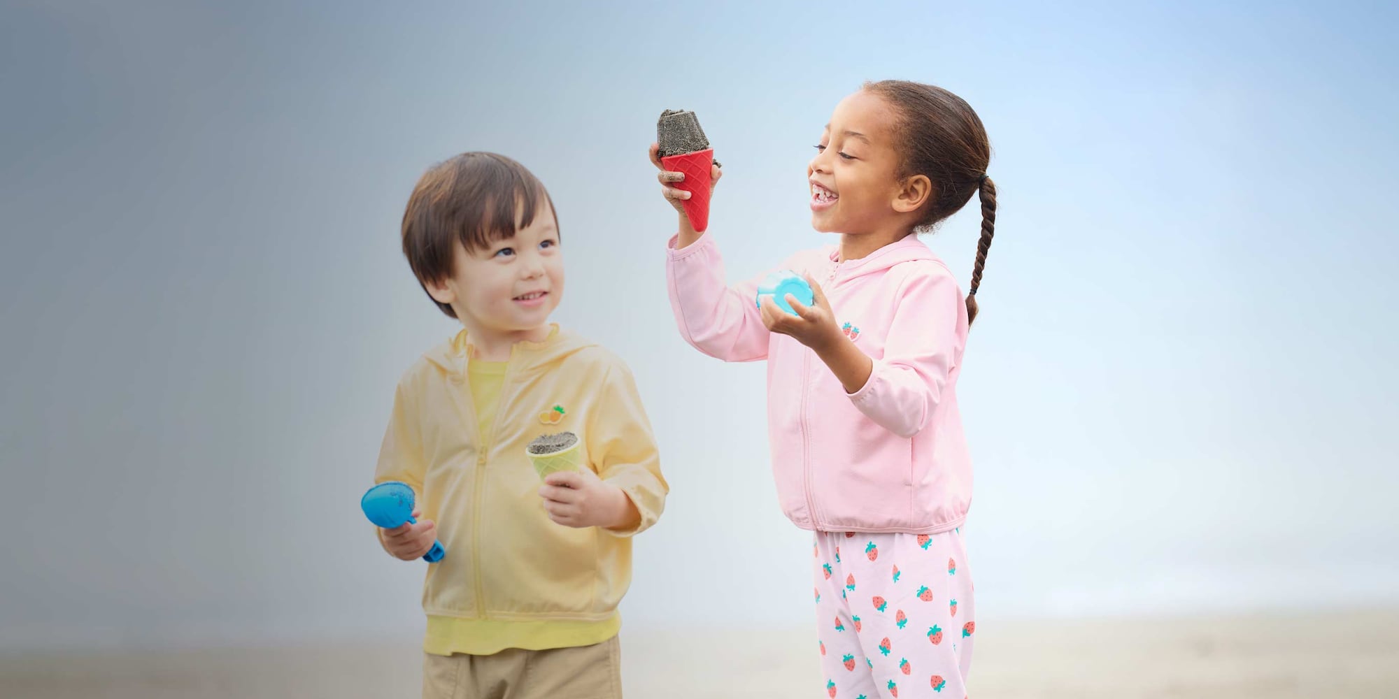 two models wearing UV Protection Mesh Hoodies in yellow and pink while playing in the sand on the beach
