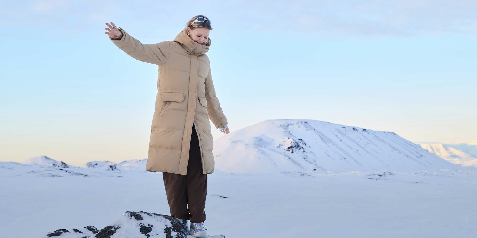 @holliemercedes wearing Ultra Warm Down Long Coat in beige with brown trousers and sunglasses in Iceland