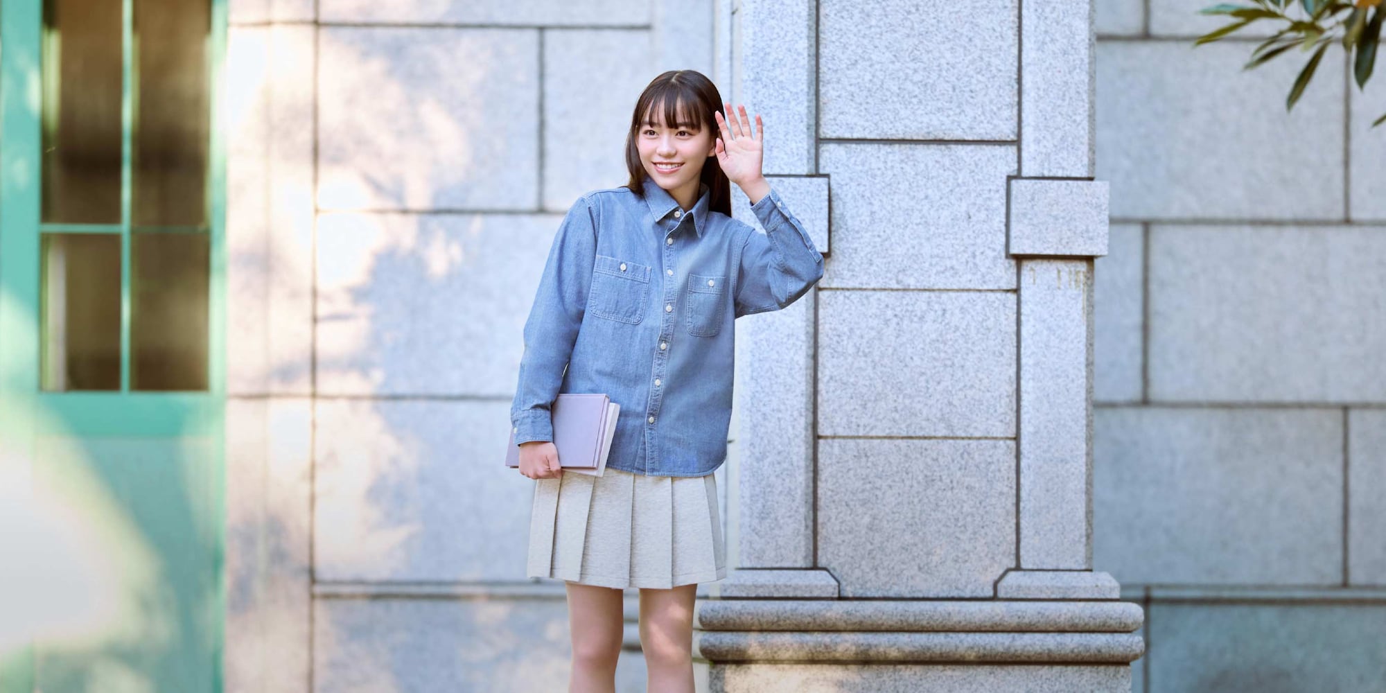 Model trägt hellgrauen Miniskort mit Falten und blaues Jeanshemd.