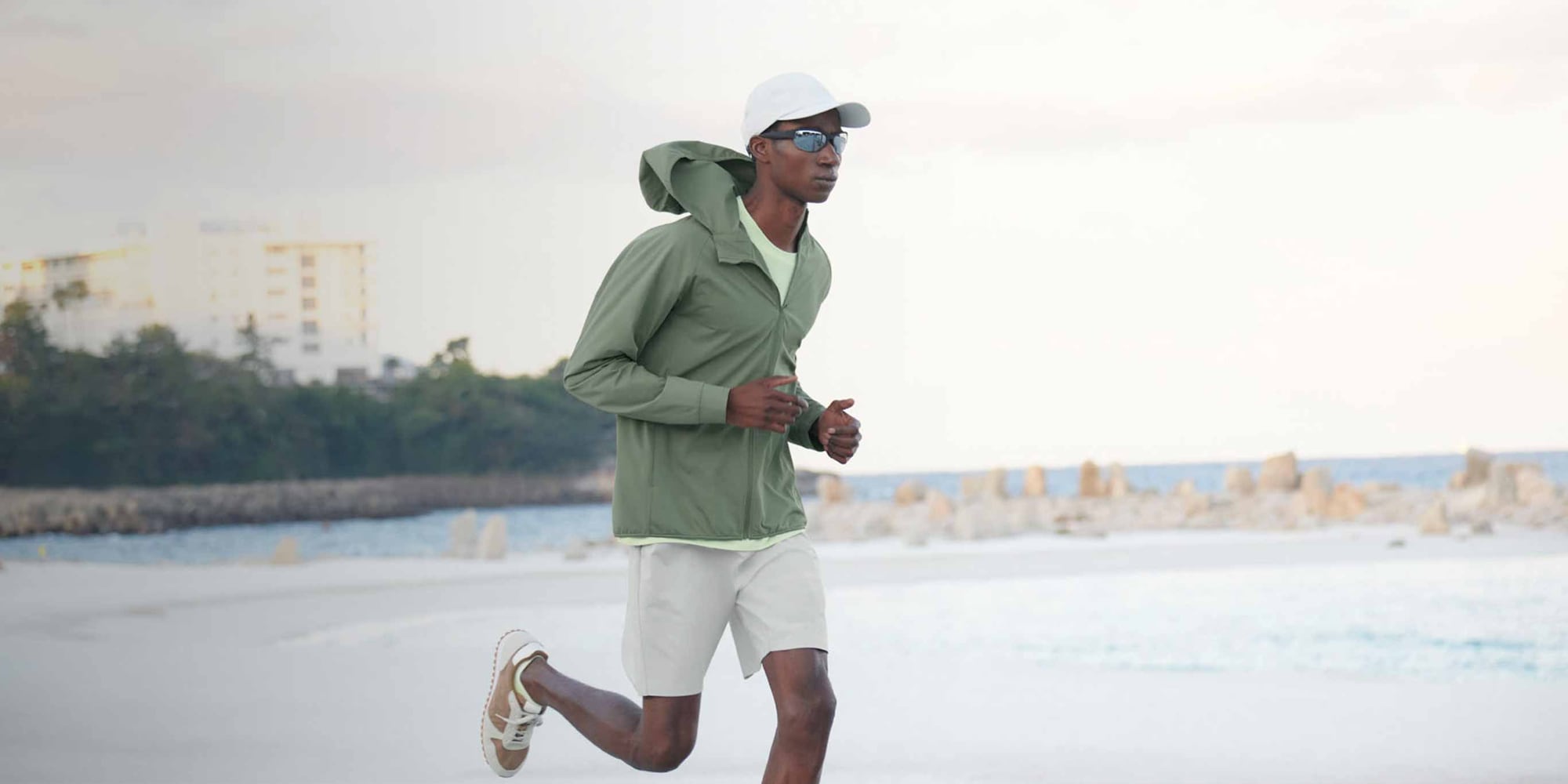 model wearing DRY-EX UV Protection Full-Zip Hoodie in olive with pale green T-shirt and off white shorts while running on the coast