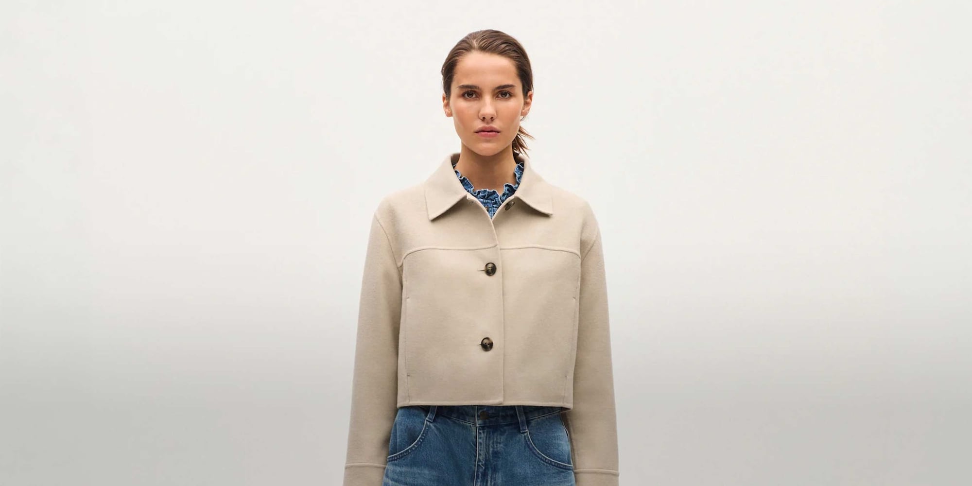 model wearing a beige cropped jacket with faded blue jeans