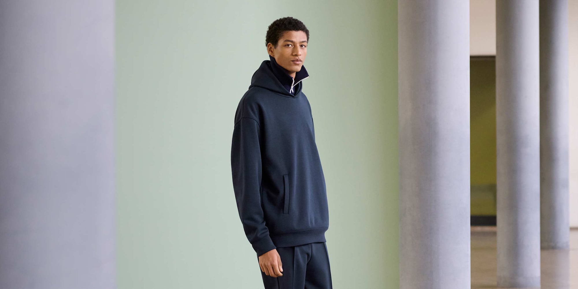 Model draagt ​​een oversized sweater met capuchon in marineblauw over een marineblauwe top met rits en een bijpassende broek.