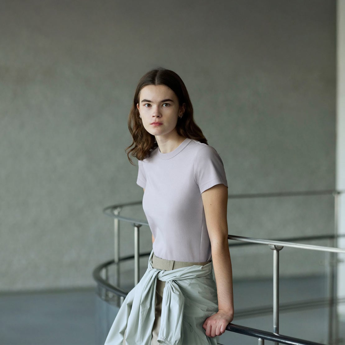 model wears a lilac Crew Neck T-Shirt with green trousers and a light blue parka wrapped around her waist