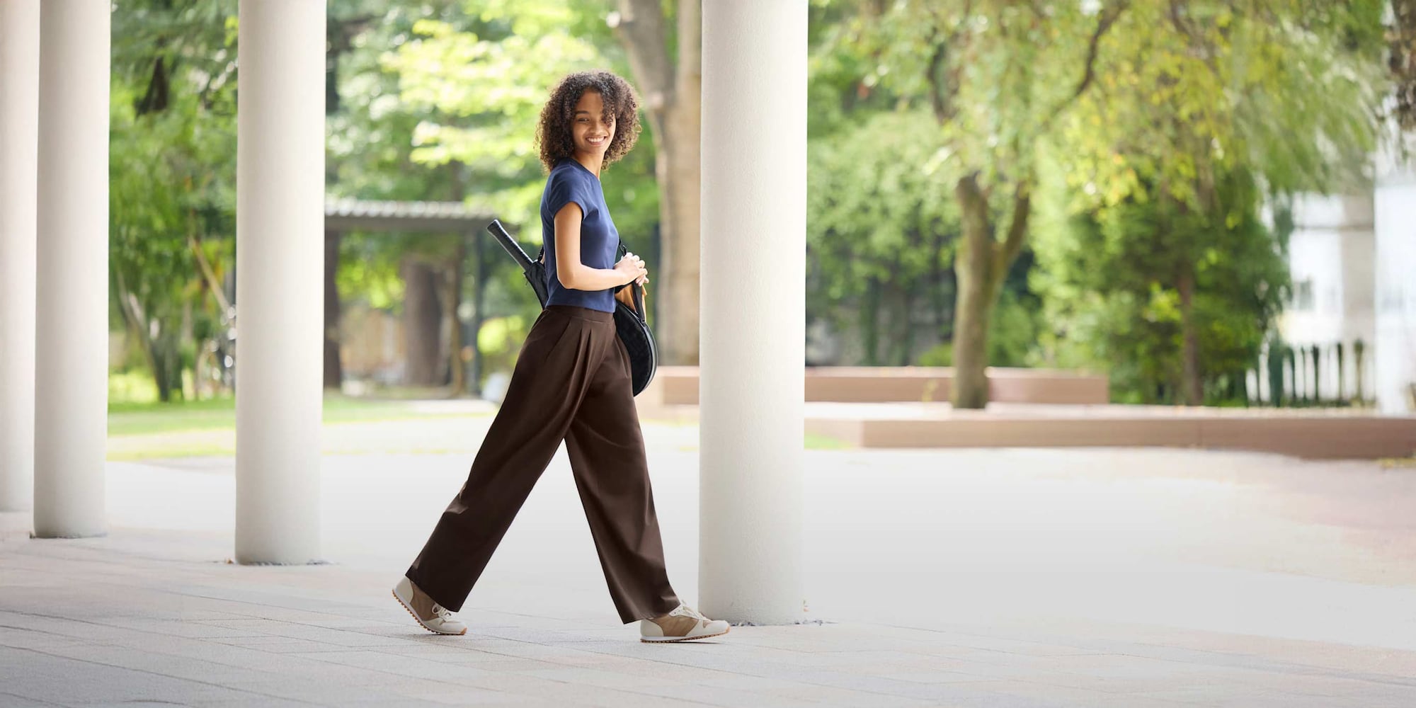 model wearing Ultra Stretch Active Wide Trousers in dark brown with a navy T-shirt while carrying a tennis racket