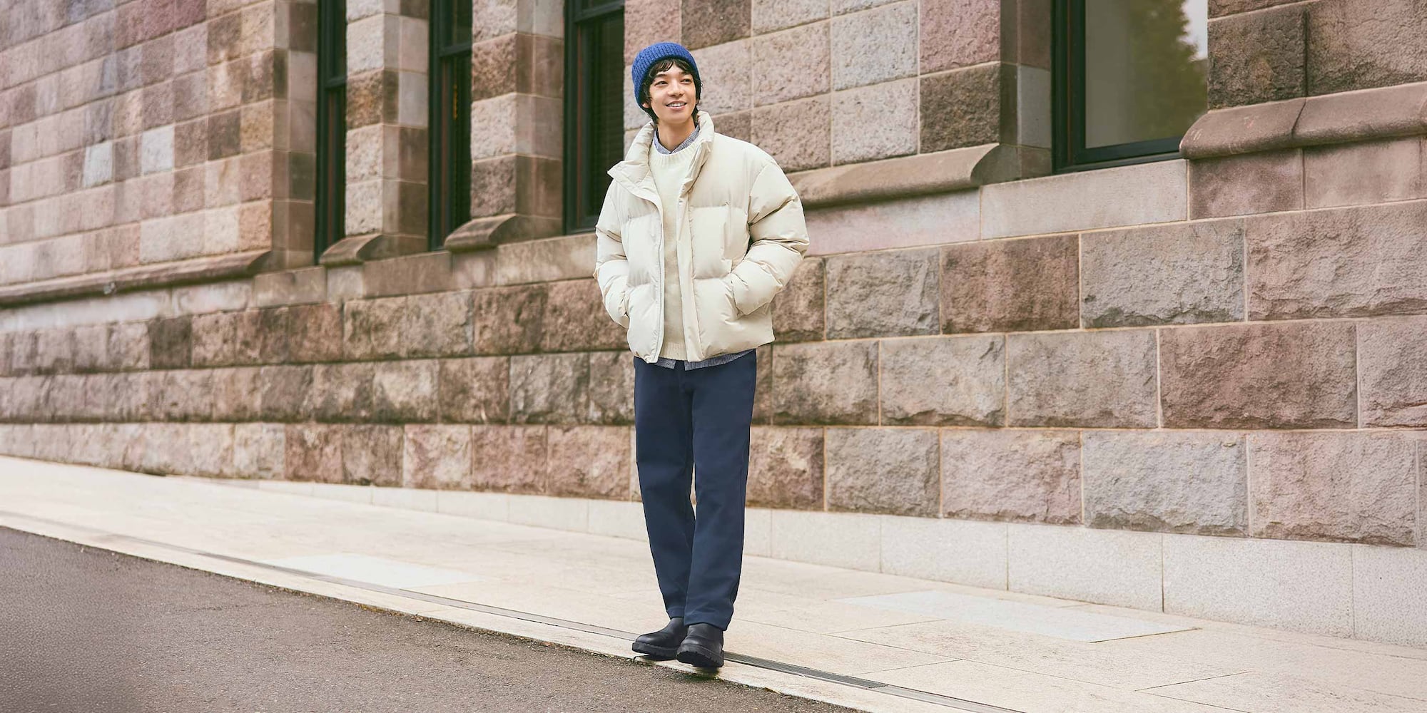 model wearing Warm Stretch Trousers in navy with an off white knit and down jacket, blue beanie and black shoes