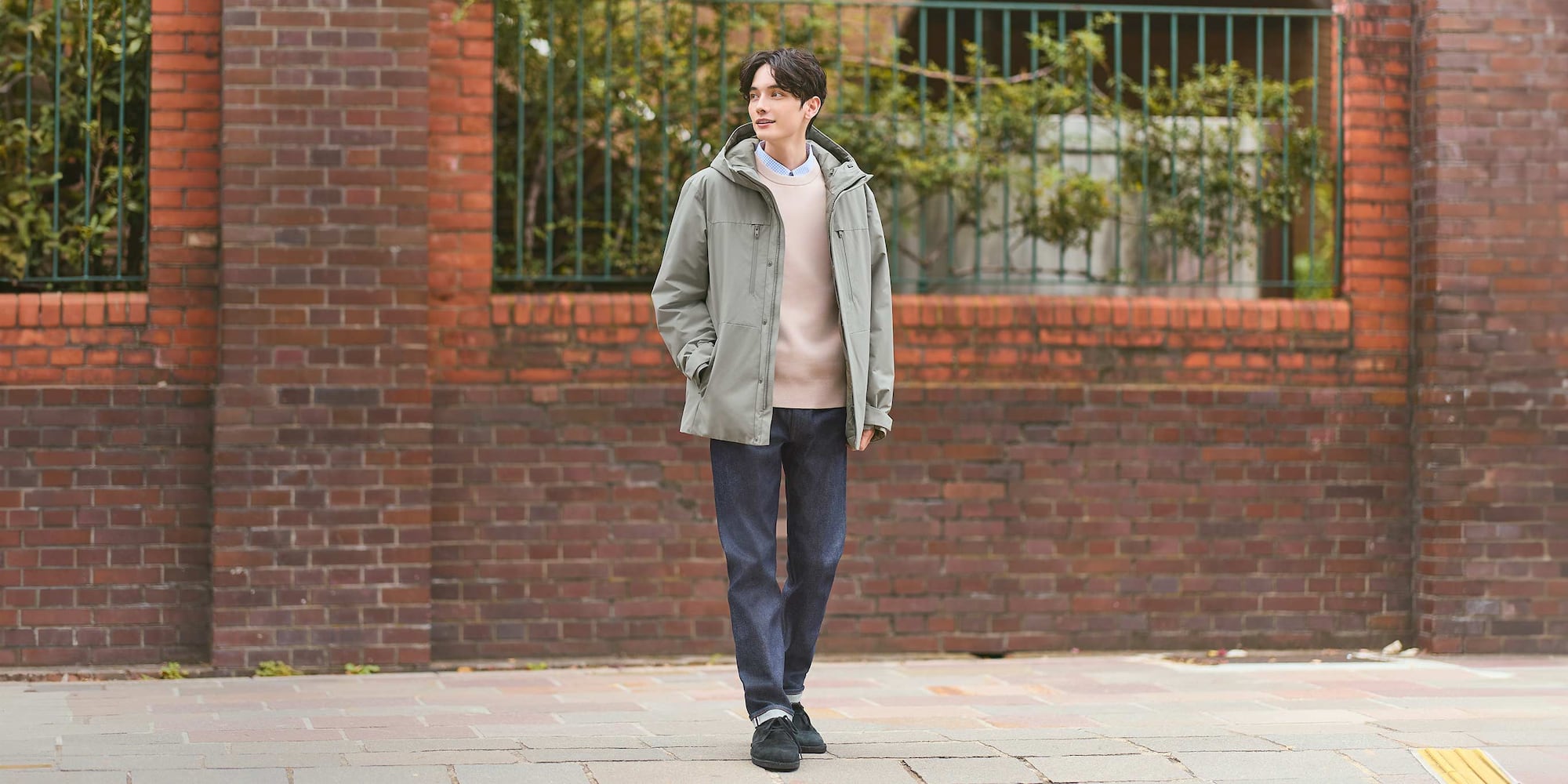 Model trägt eine schmale, gerade geschnittene Jeans mit Webkante, dazu ein hellblaues Karohemd, einen beigen Pullover und eine grüne Jacke.