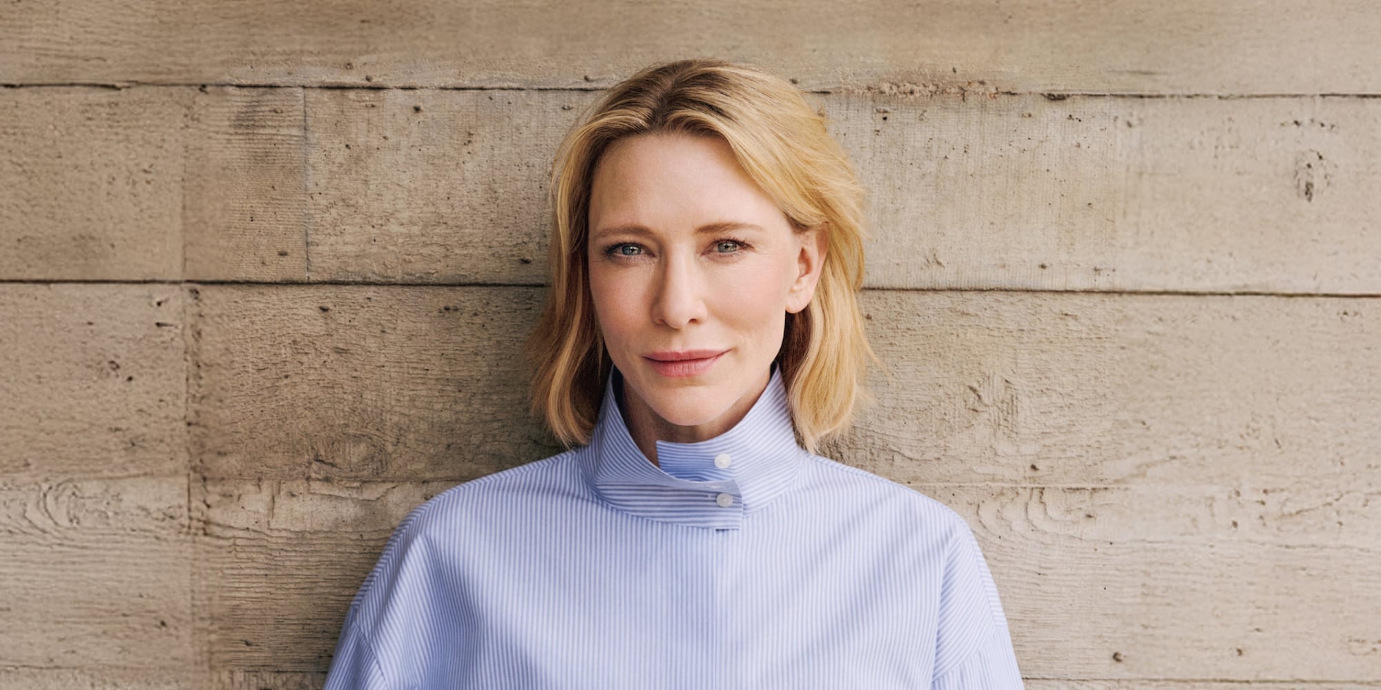 Cate Blanchett wearing a blue and white striped shirt against a wooden background