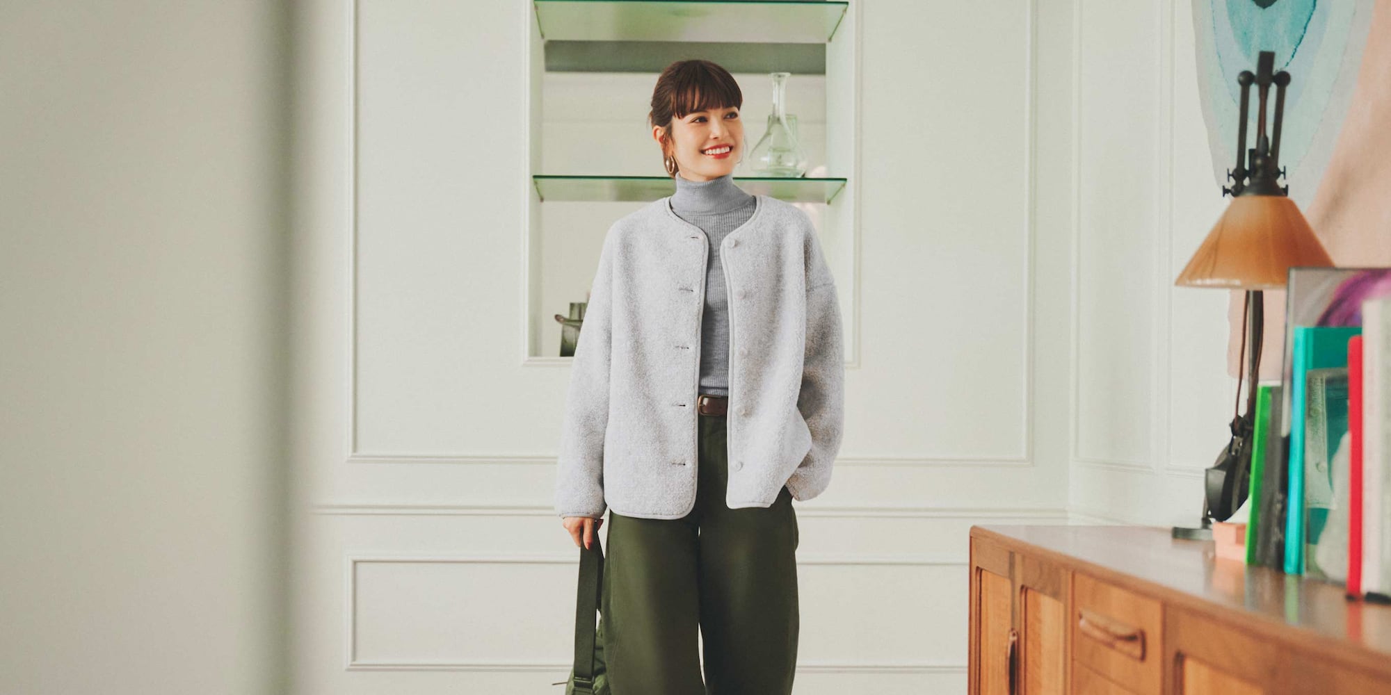 model wearing Pile Lined Fleece Relaxed Cardigan in light grey with a grey turtleneck, green trousers, brown belt and gold hoops