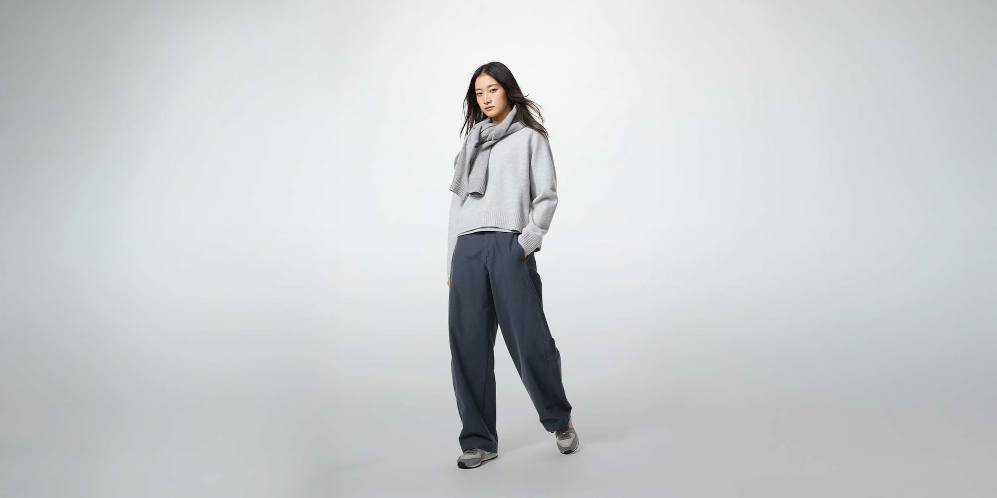 model wearing Jersey Barrel Leg Trousers in dark grey with a light grey knit and trainers