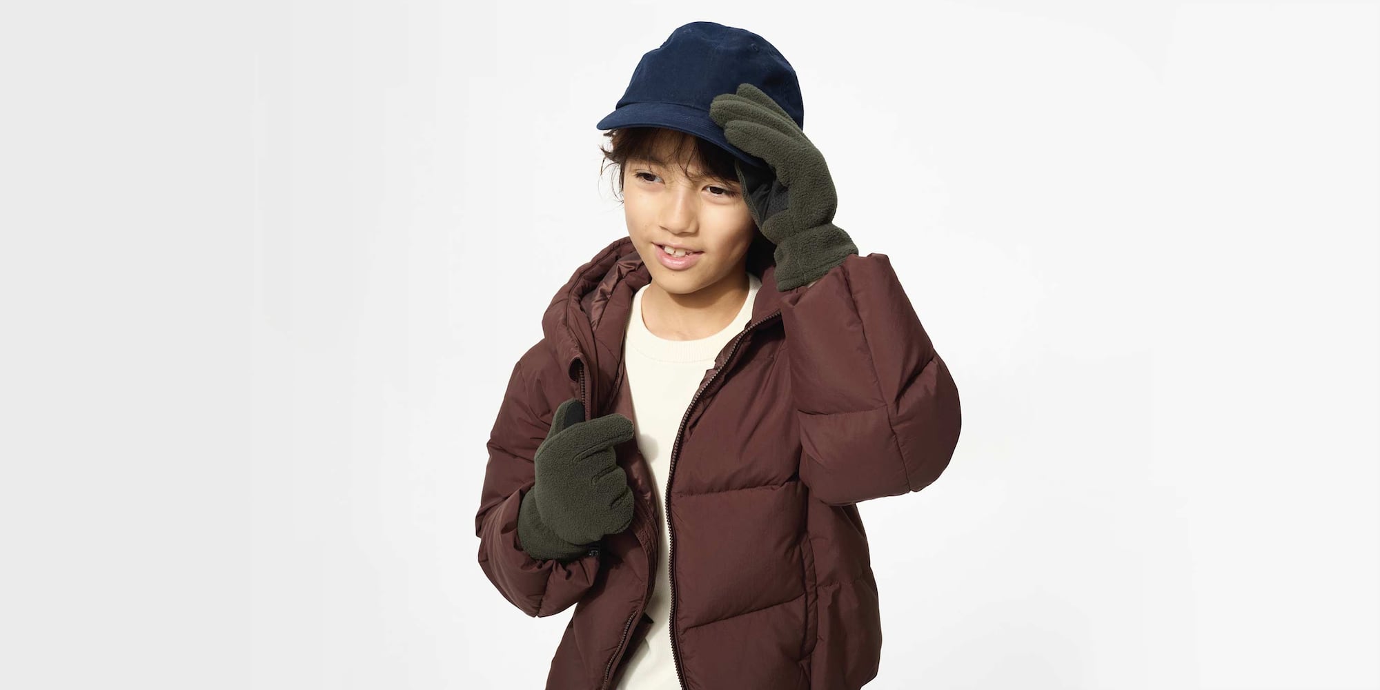 Model trägt dunkelgrüne Handschuhe mit HEATTECH-Futter, dazu eine marineblaue Baseballkappe, eine braune Jacke und ein weißes Oberteil.