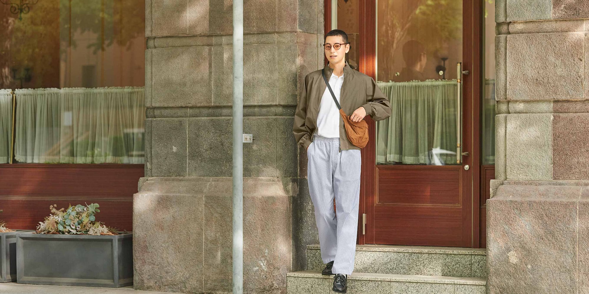 model wearing Stretch Easy Ankle Trousers in blue with a white polo shirt, brown jacket and brown bag
