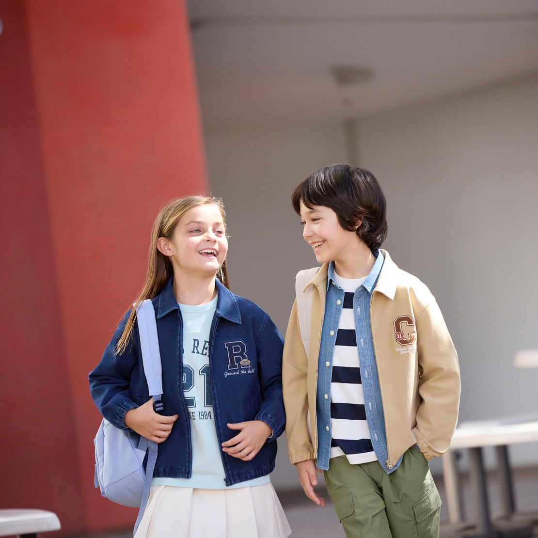 Two kids outdoors wearing light jackets and casual tops, holding water bottles.