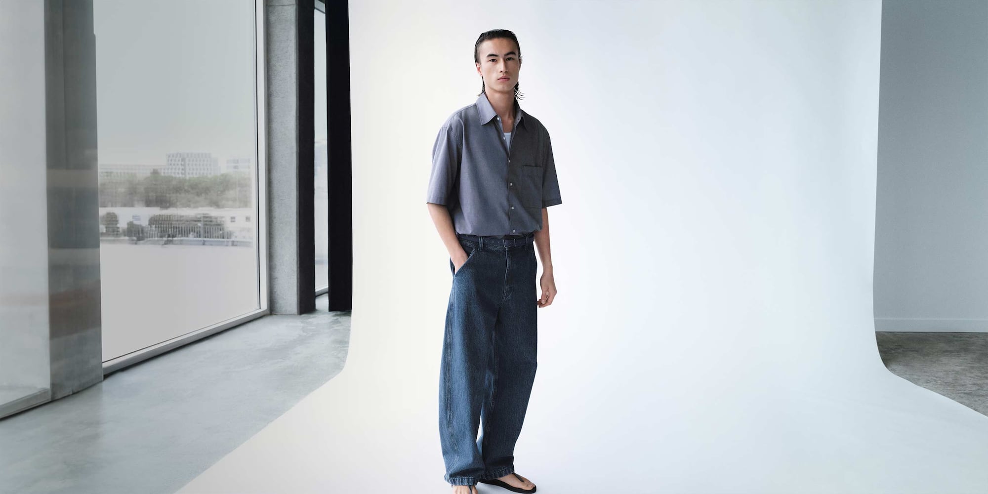 model wearing a grey short sleeved shirt over a white tank top with dark wash jeans