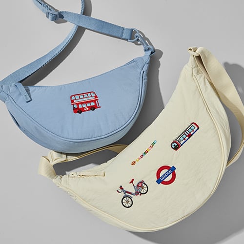 two round mini shoulder bags; one light blue featuring embroidery of a London bus and one cream featuring embroidery of the London underground logo in rainbow colours, a "Boris" bike, a London underground roundel and a tube carriage
