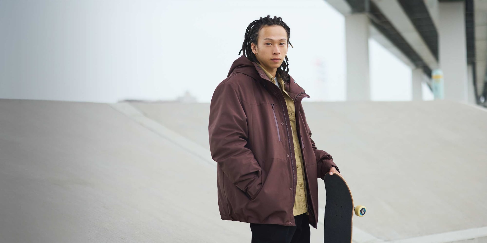 Ayumu Hirano wearing hybrid down parka in wine over a beige shirt while holding a skateboard