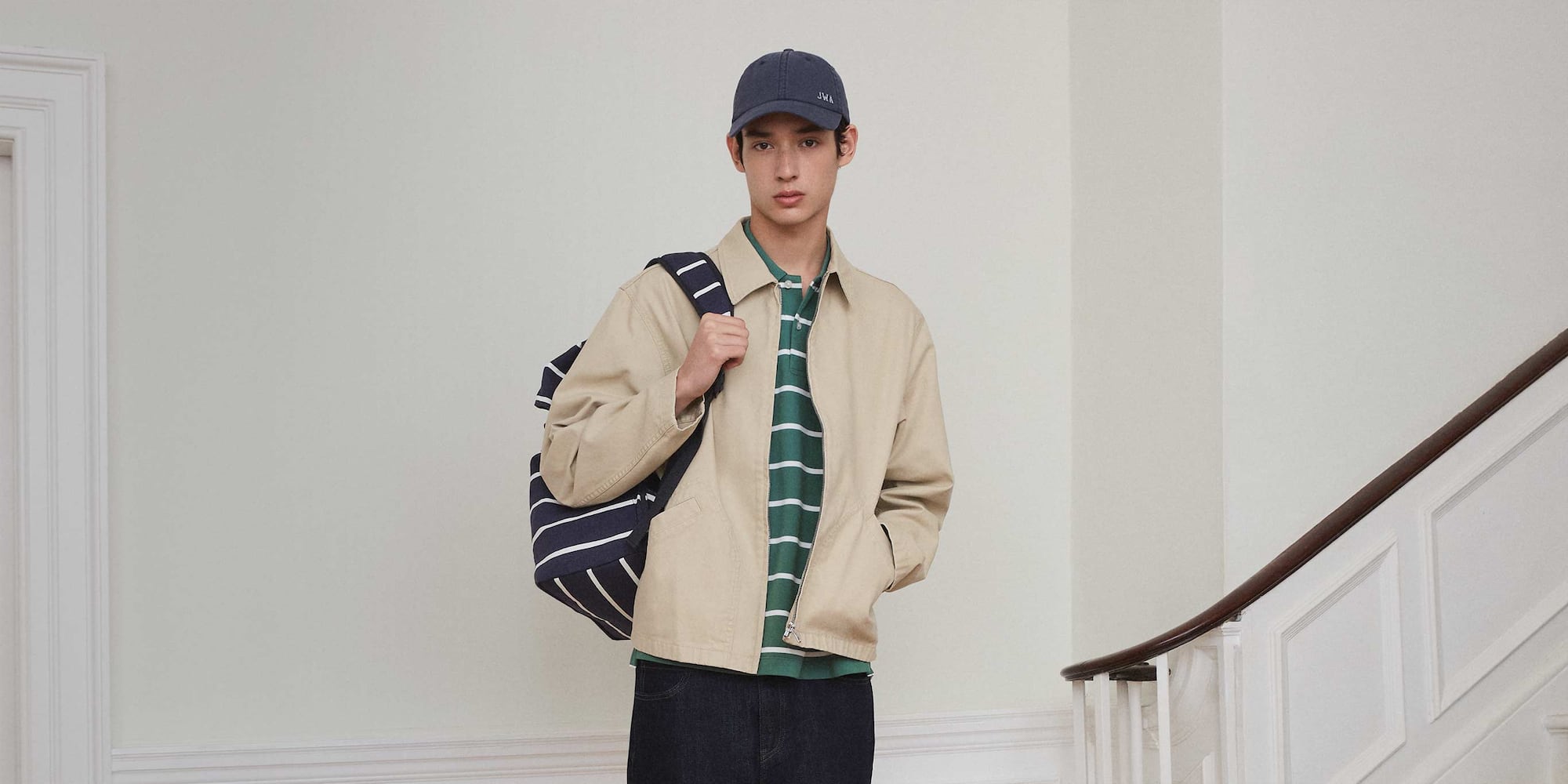 model wearing Zip-Up Blouson in beige with a green and white striped polo shirt, jeans, navy and white striped backpack and blue cap