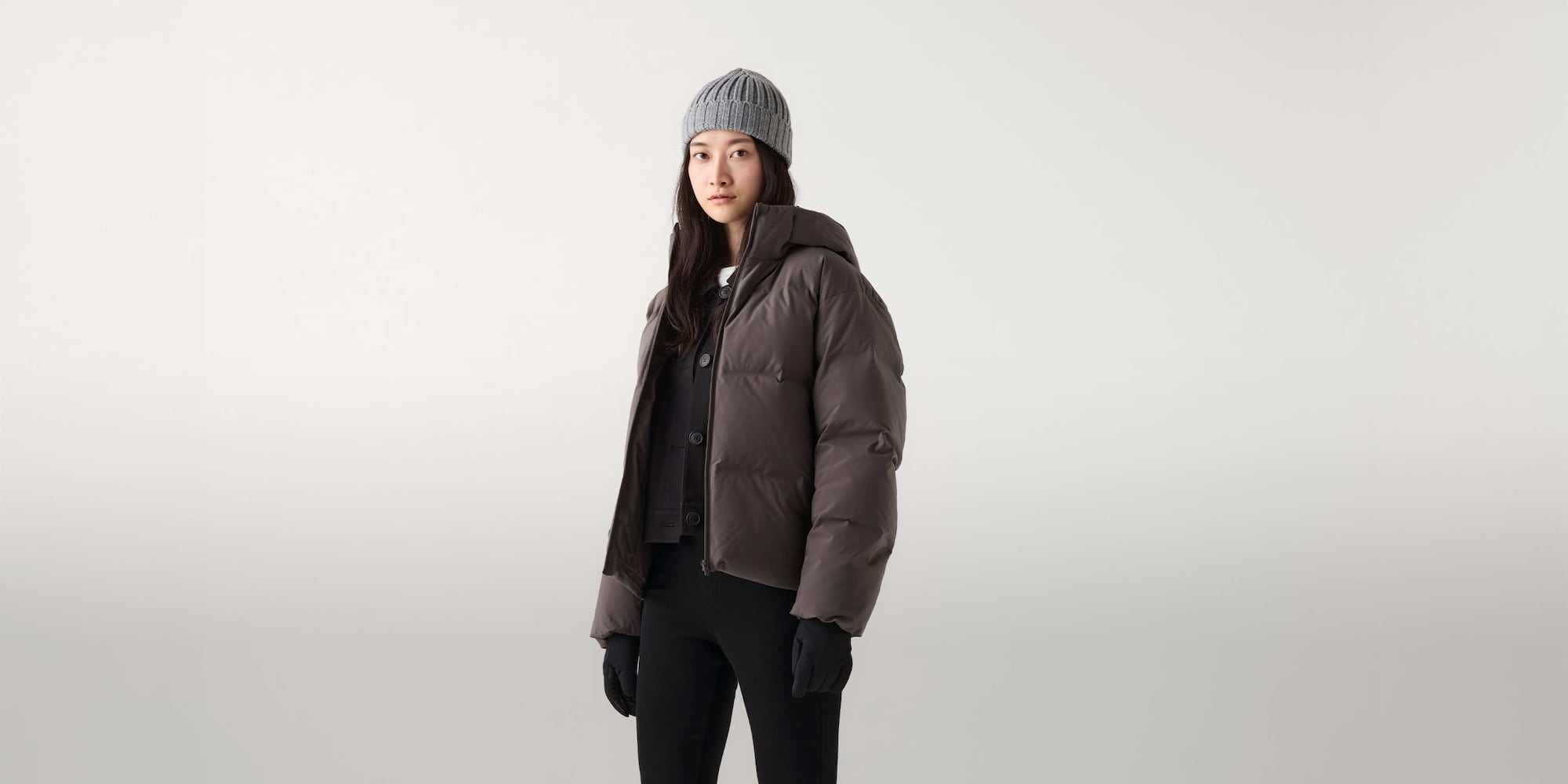 a model wearing Seamless Down Parka in grey over a black knit and trousers with a grey beanie and black gloves