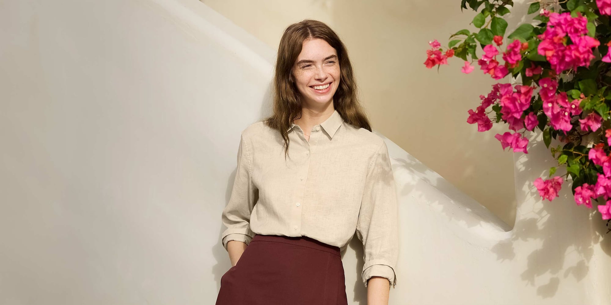 a model leans against a wall wearing a stone linen shirt and a wine skirt