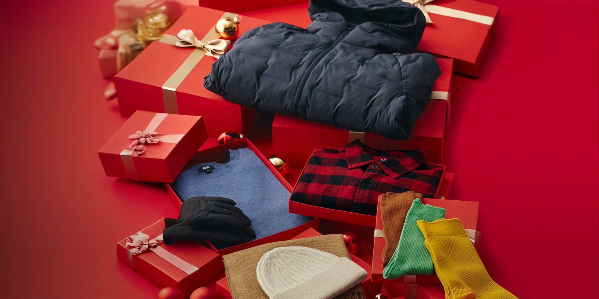 Zwei Models, die UNIQLO-Mützen, -Schals und -Handschuhe tragen und verpackte Geschenke halten