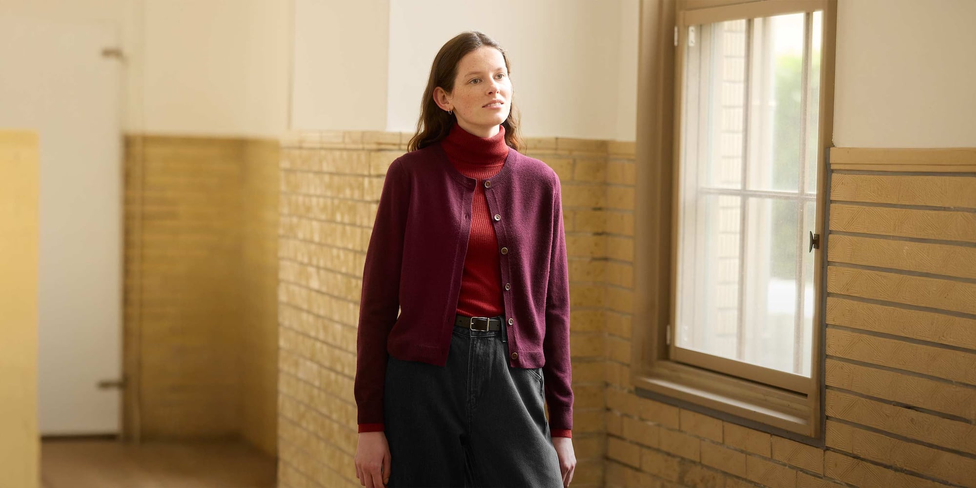 model wearing 100% Crew Neck Short Cardigan in red over a red turtleneck with dark grey jeans