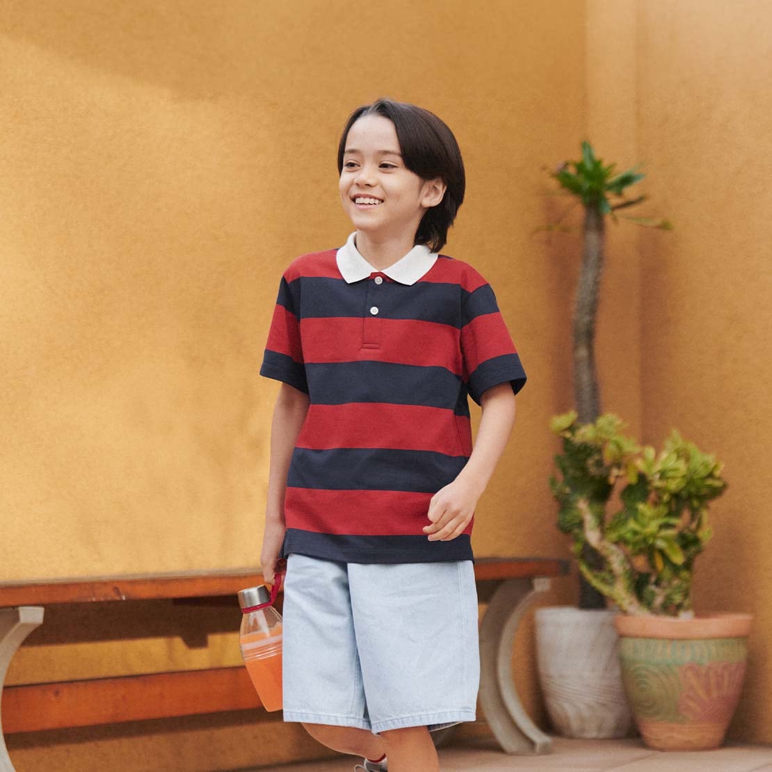 model wearing DRY Piqué Polo Shirt in red with light blue shorts, carrying a drink bottle