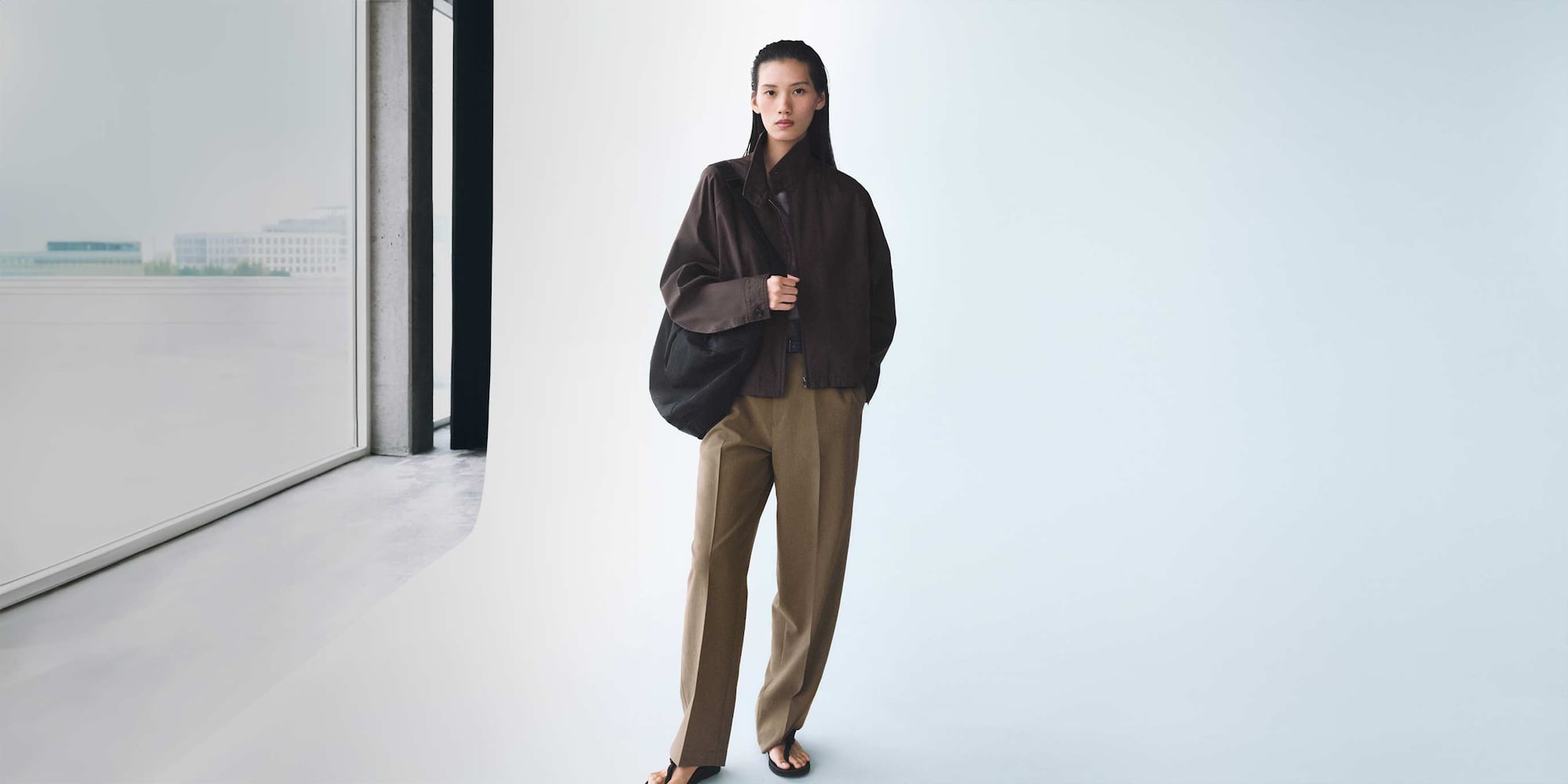 model wearing dark brown jacket, light brown trousers and a black shoulder bag