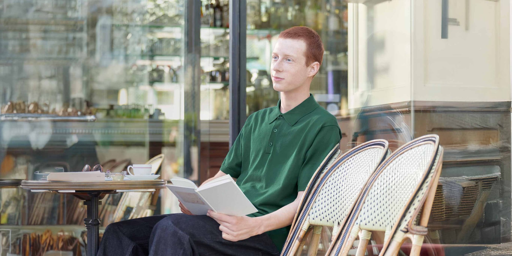 model wearing Washable Knit Polo Jumper in green with dark wash jeans while sat outside a café reading a book