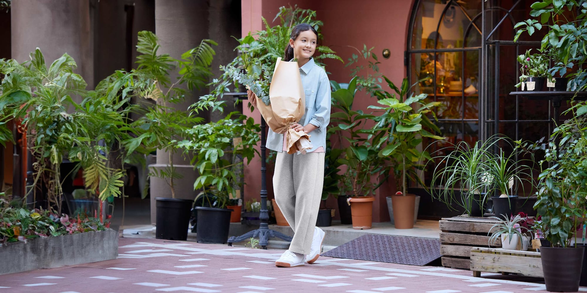 Model trägt hellgraue Jogginghose, hellblaues Hemd und einen Blumenstrauß.