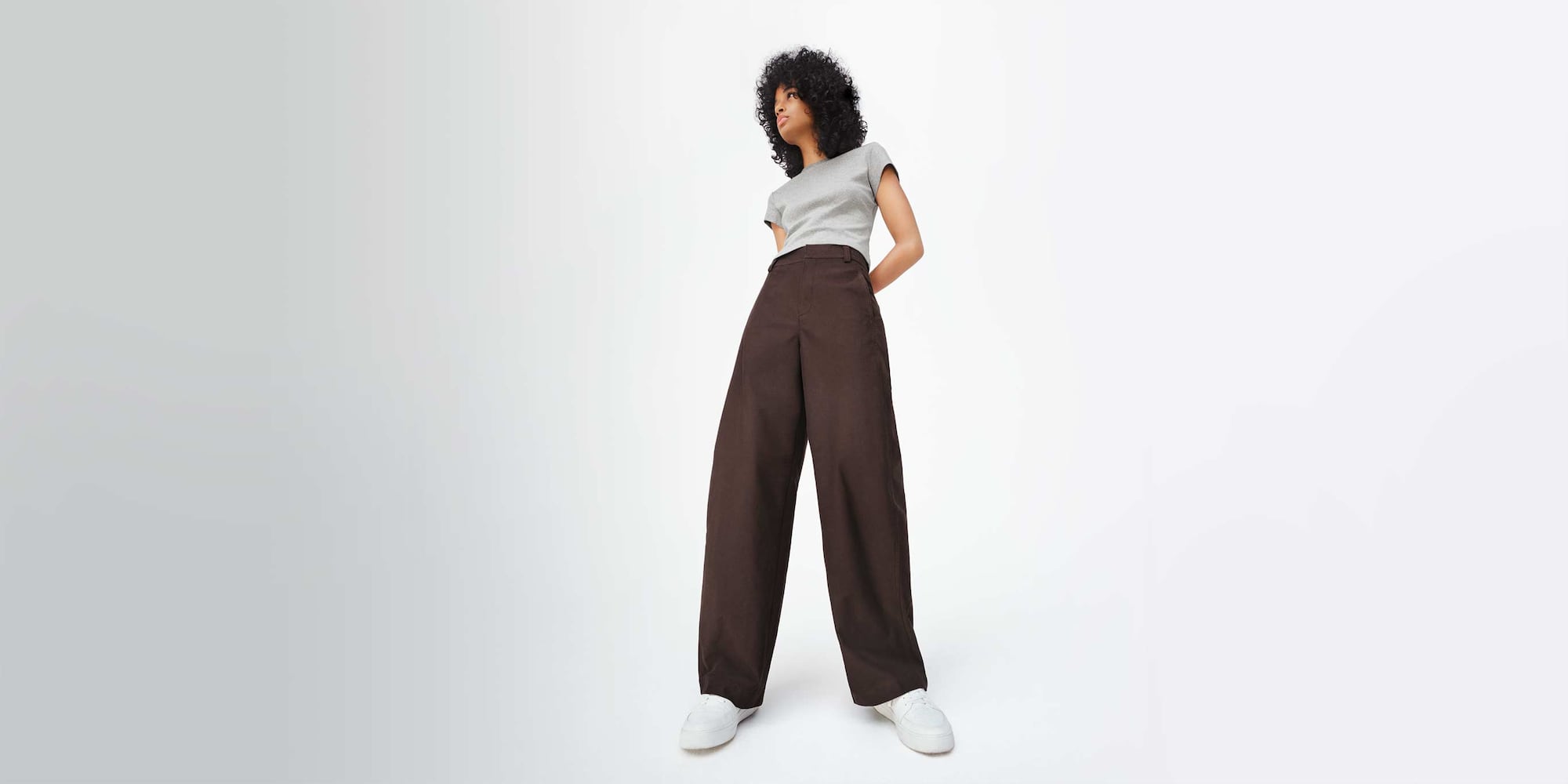 model wearing Jersey Barrel Leg Trousers in dark brown with a grey T-shirt and white trainers