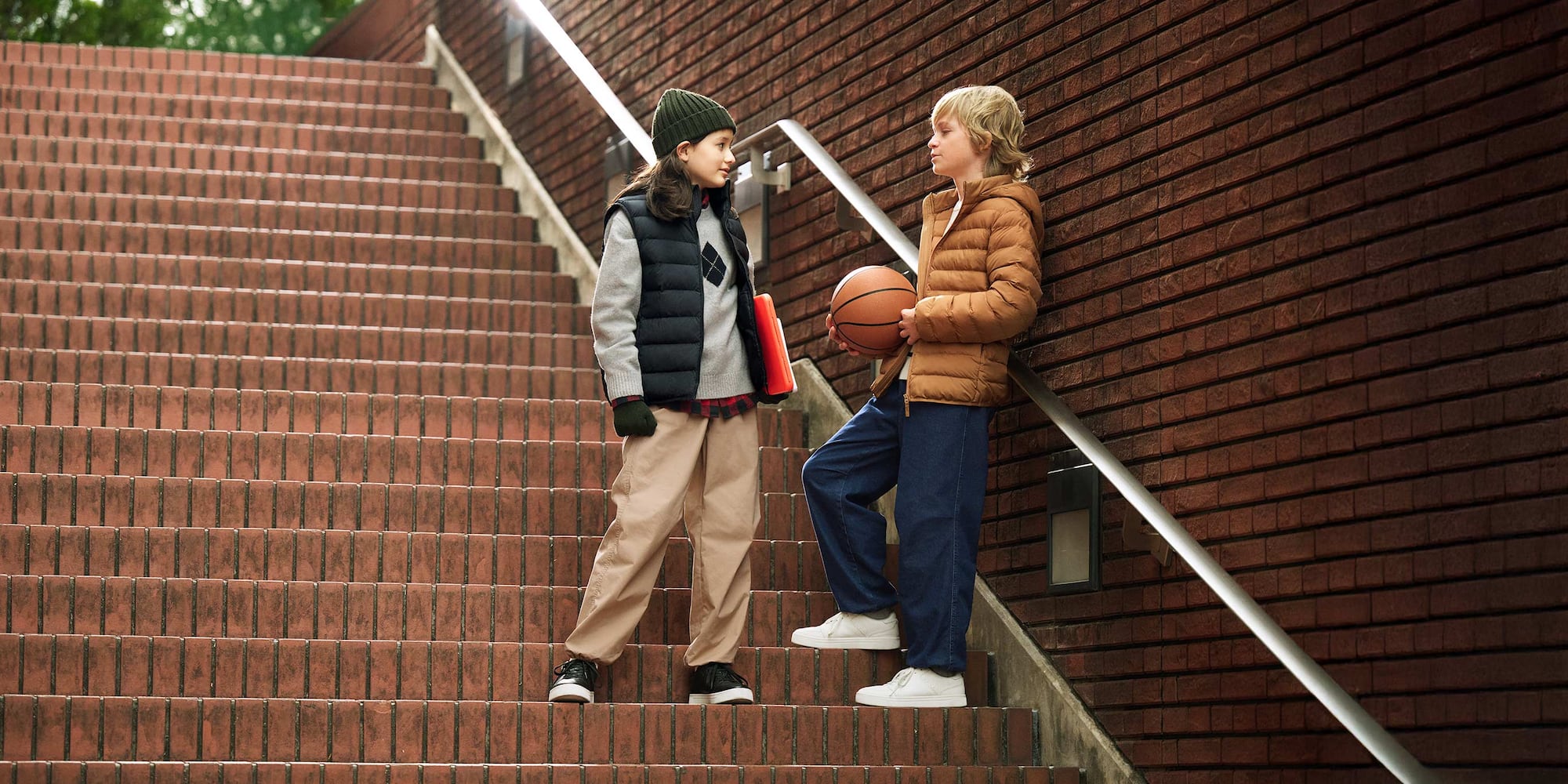 two models, one wearing Warm Lined Trousers in beige with a red and black checked shirt, grey fair isle knit, navy puffer vest, green beanie and black glvoes and trainers