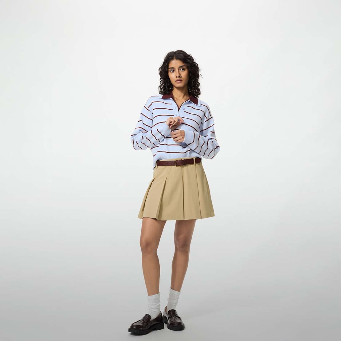 model wearing Pleated Skort in beige with a light blue and maroon knitted polo and a brown belt, white socks and black loafers