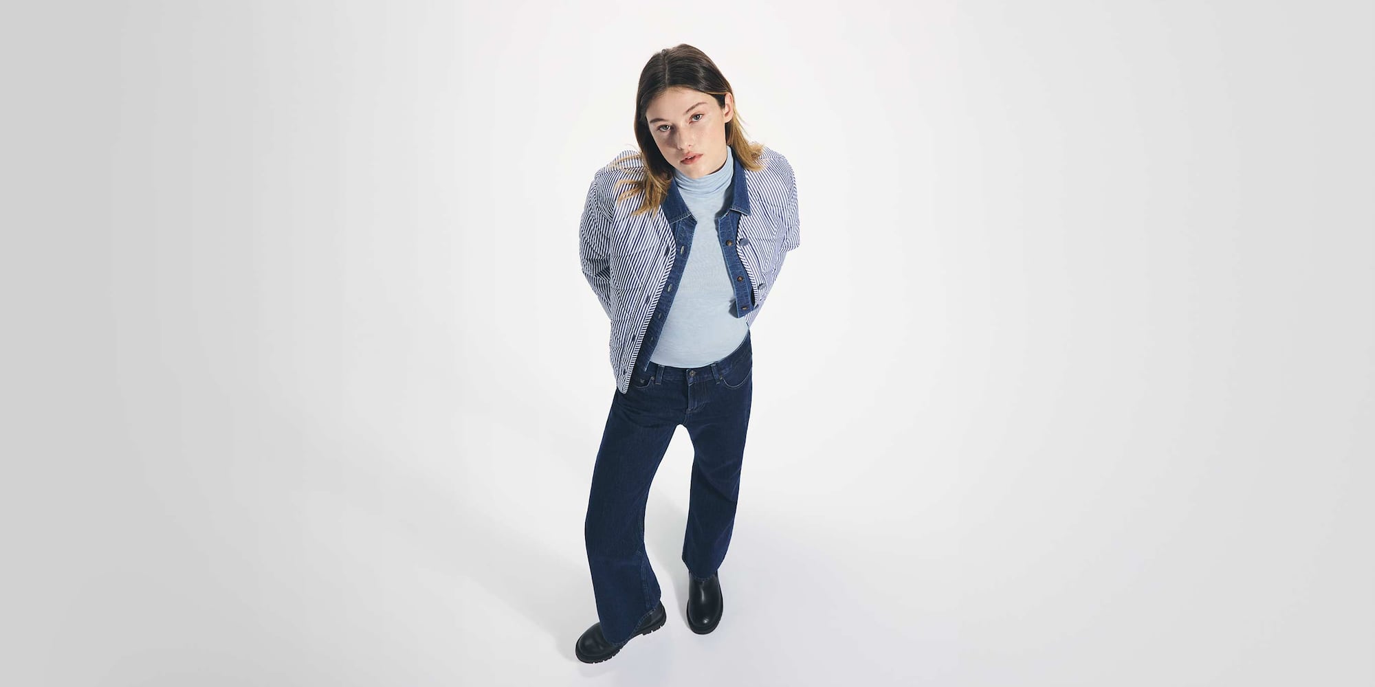 model wearing HEATTECH Extra Warm Cashmere Blend* Turtleneck T-Shirt in grey under a denim shirt and blue and white striped jacket with dark wash jeans and black boots