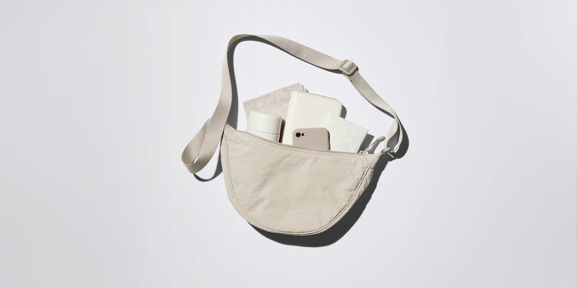 A cream coloured Round Mini Shoulder Bag laying on a white background with a plethora of items inside including a phone, water bottle and purse