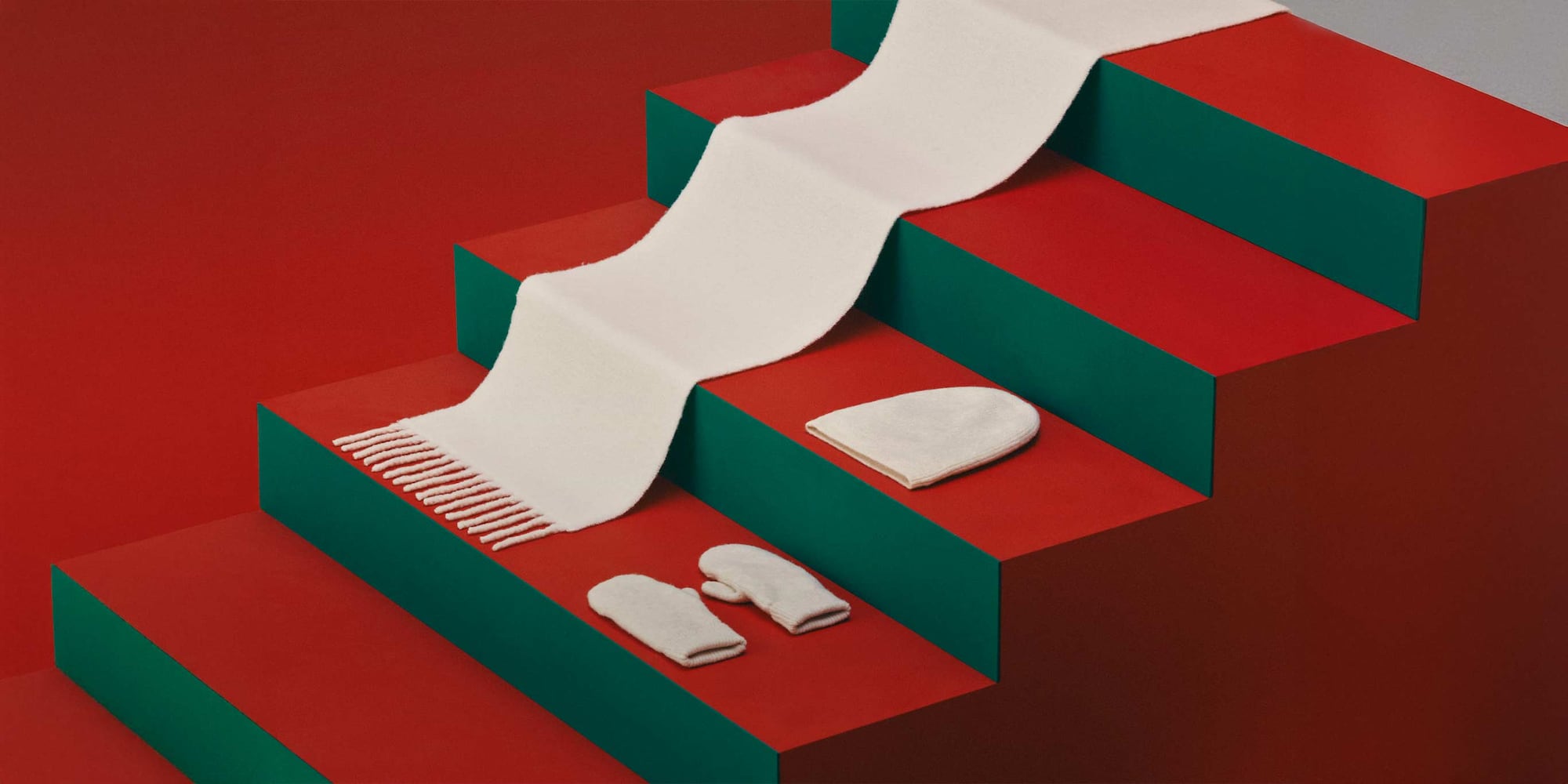 an off white scarf, hat and gloves arranged on red and green steps