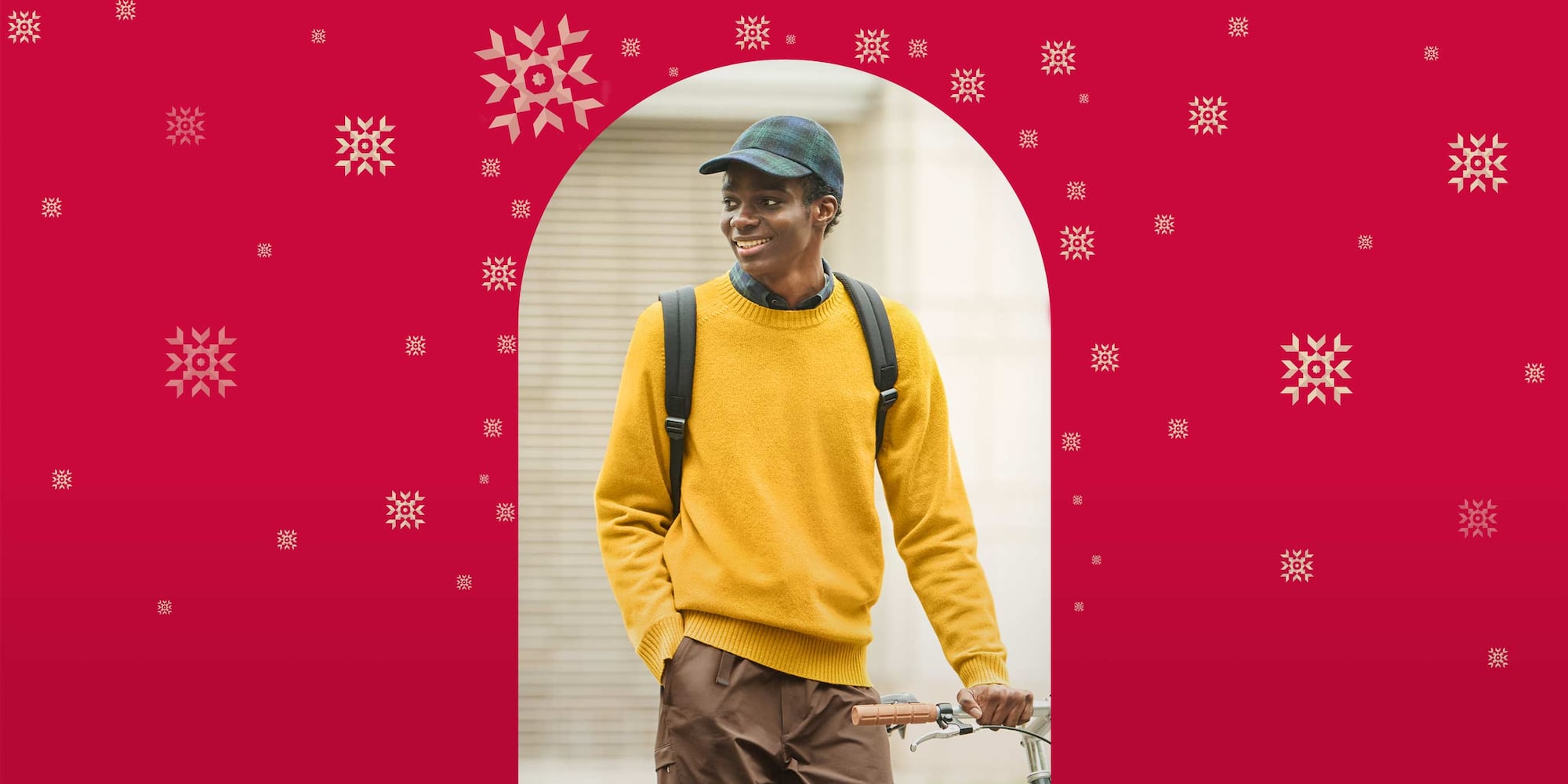 model wearing Lambswool Crew Neck Jumper in yellow over a navy checked shirt with brown trousers and a tartan cap while carrying a backpack and pushing a bicycle