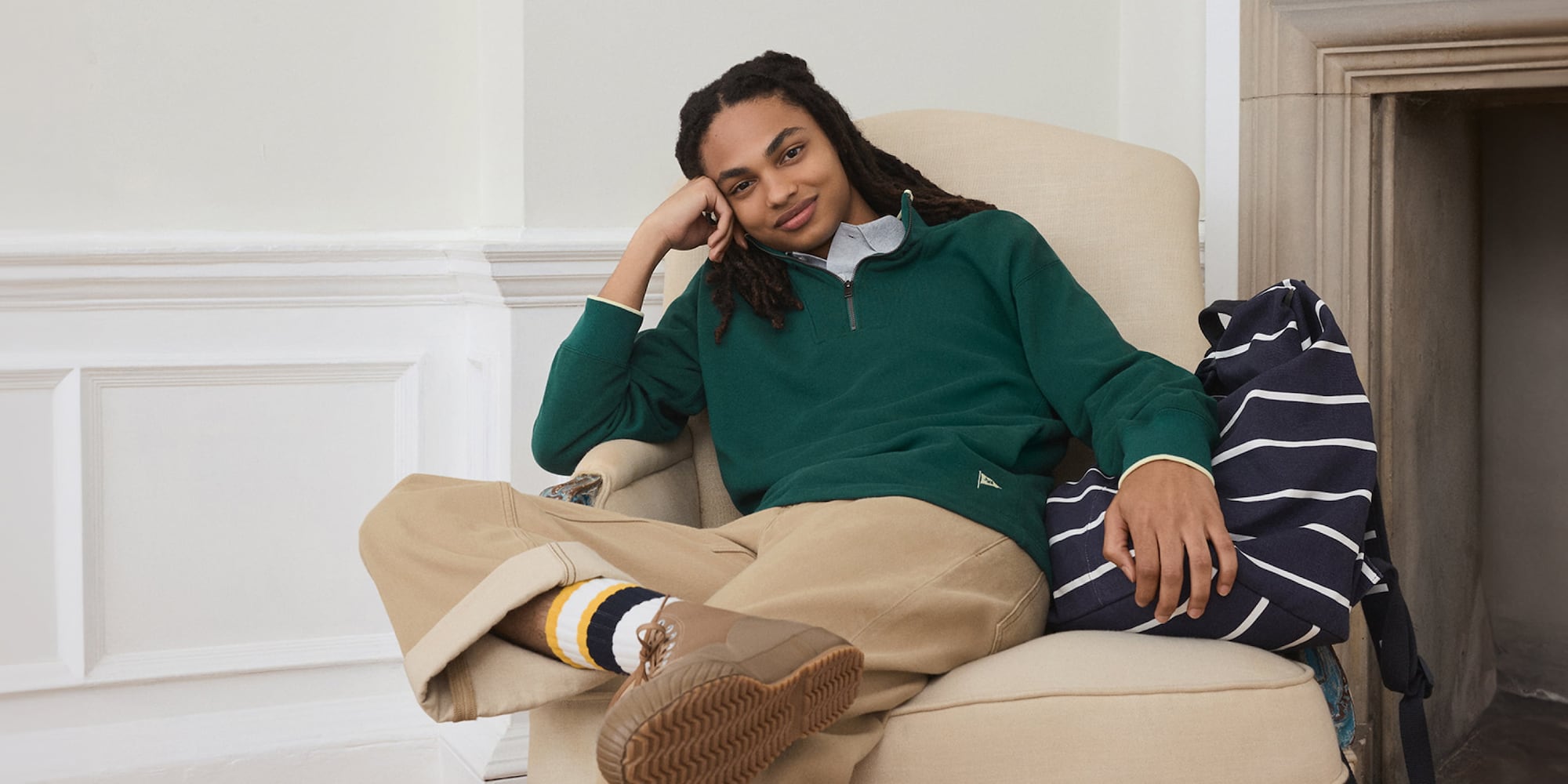 Mannequin portant un pull vert à demi-zip par-dessus une chemise, un jean beige, des chaussettes rayées et des bottes beiges.