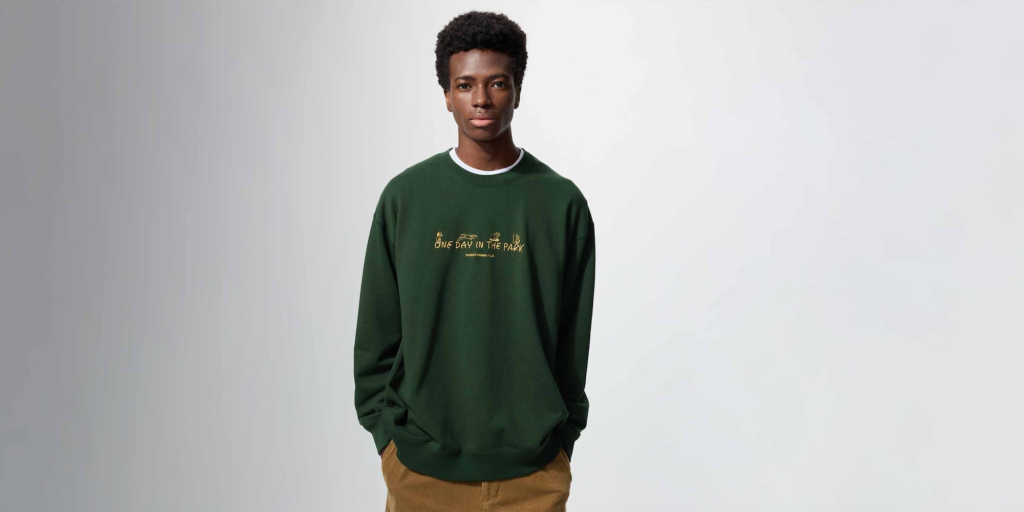 model wearing Yu Nagaba UT Graphic Sweatshirt in dark green over a white T-shirt with brown corduroy trousers