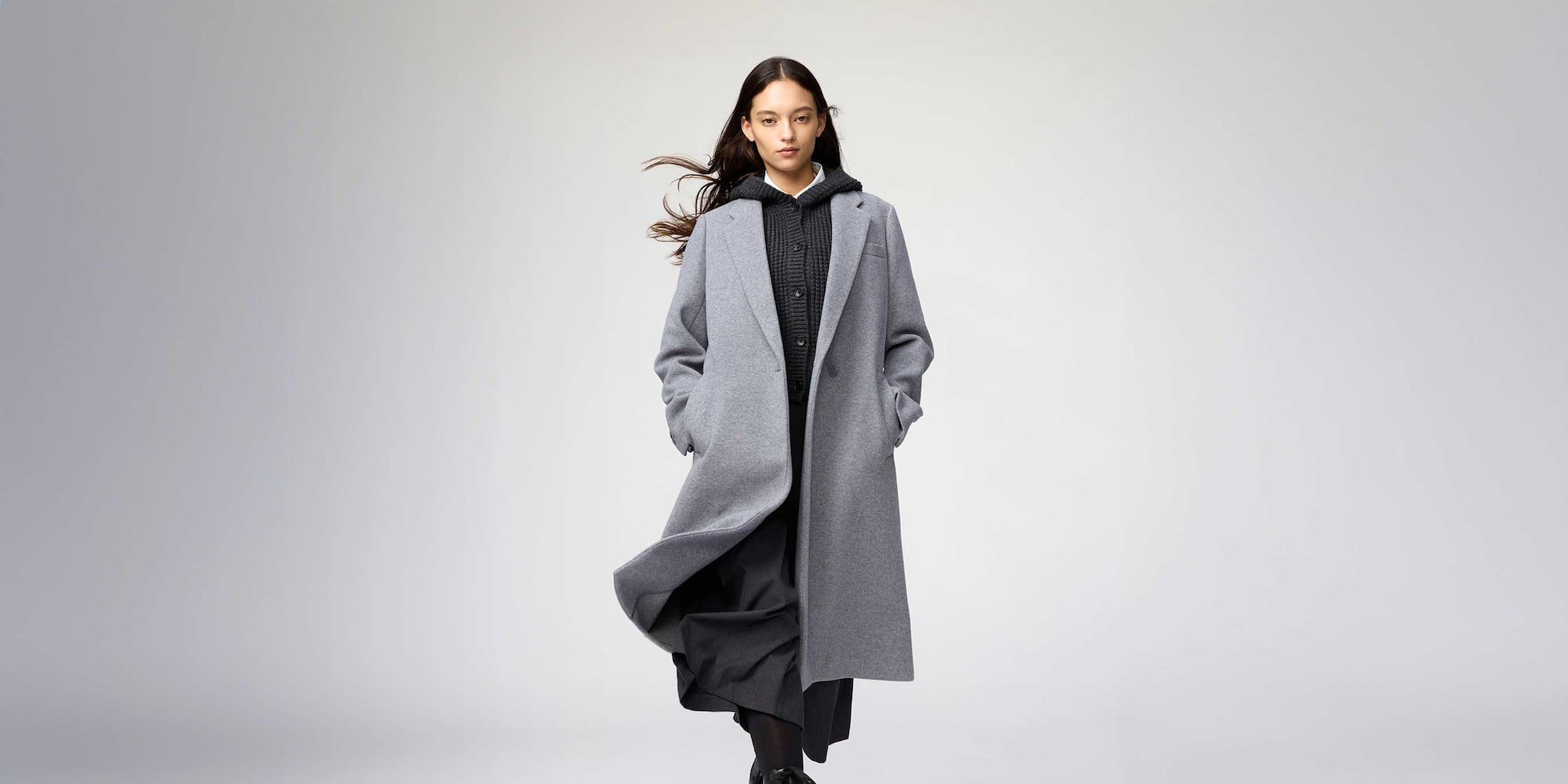 a model wearing the new grey UNIQLO : C Long Coat over a black knitted hoodie and black skirt