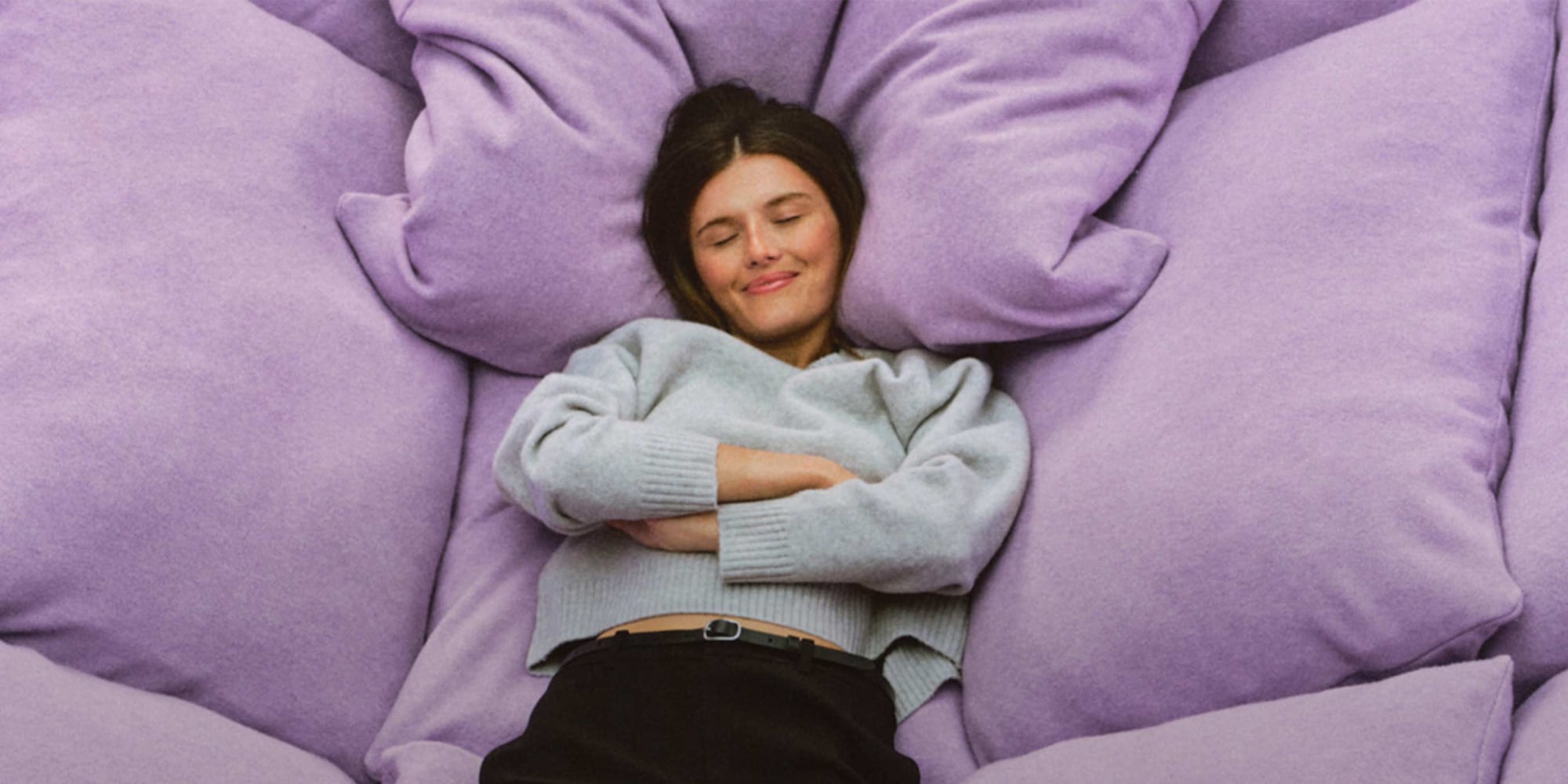 model wearing Soufflé Yarn Crew Neck Jumper in light grey, relaxing against a giant purple pillow
