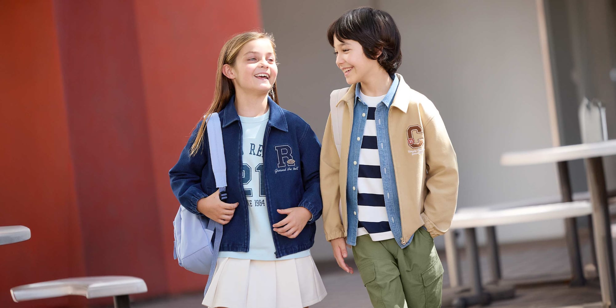 Model trägt beigefarbene Collegejacke, blaues Jeanshemd, weiß-blaugestreiftes T-Shirt und olivgrüne Cargohosen.