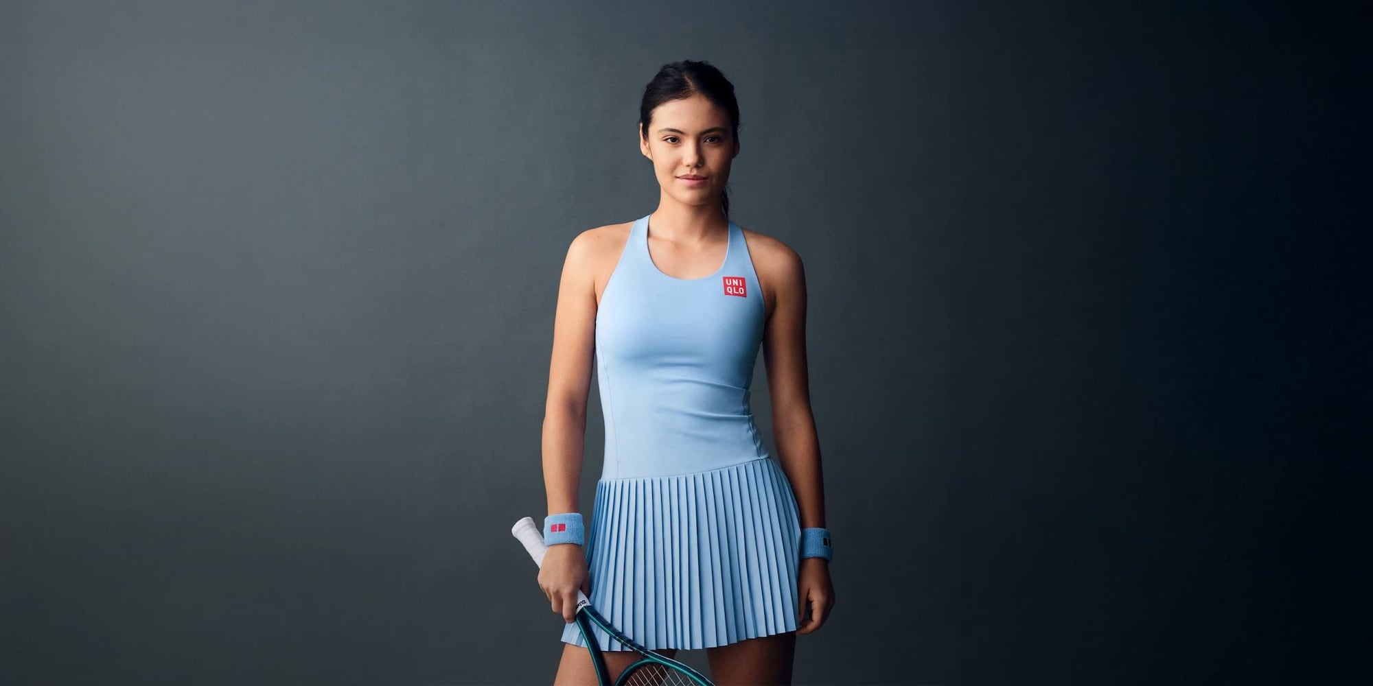 UNIQLO Global Brand Ambassador Emma Raducanu wearing light blue tennis dress and sweatbands with the uniqlo logo while holding a tennis racket
