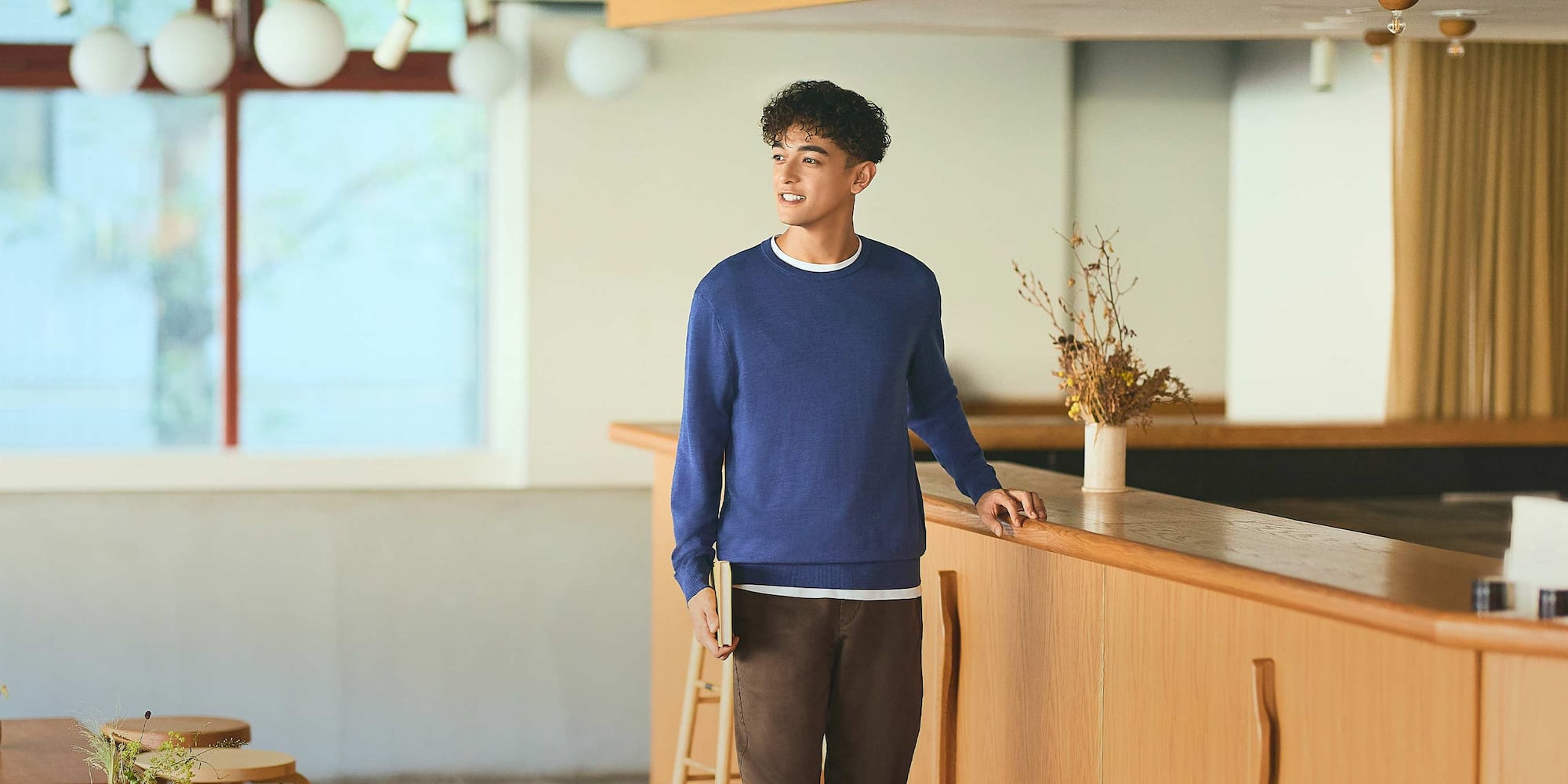 model wearing 100% Merino Crew Neck Jumper in blue over a white T-shirt with brown trousers, while holding a book